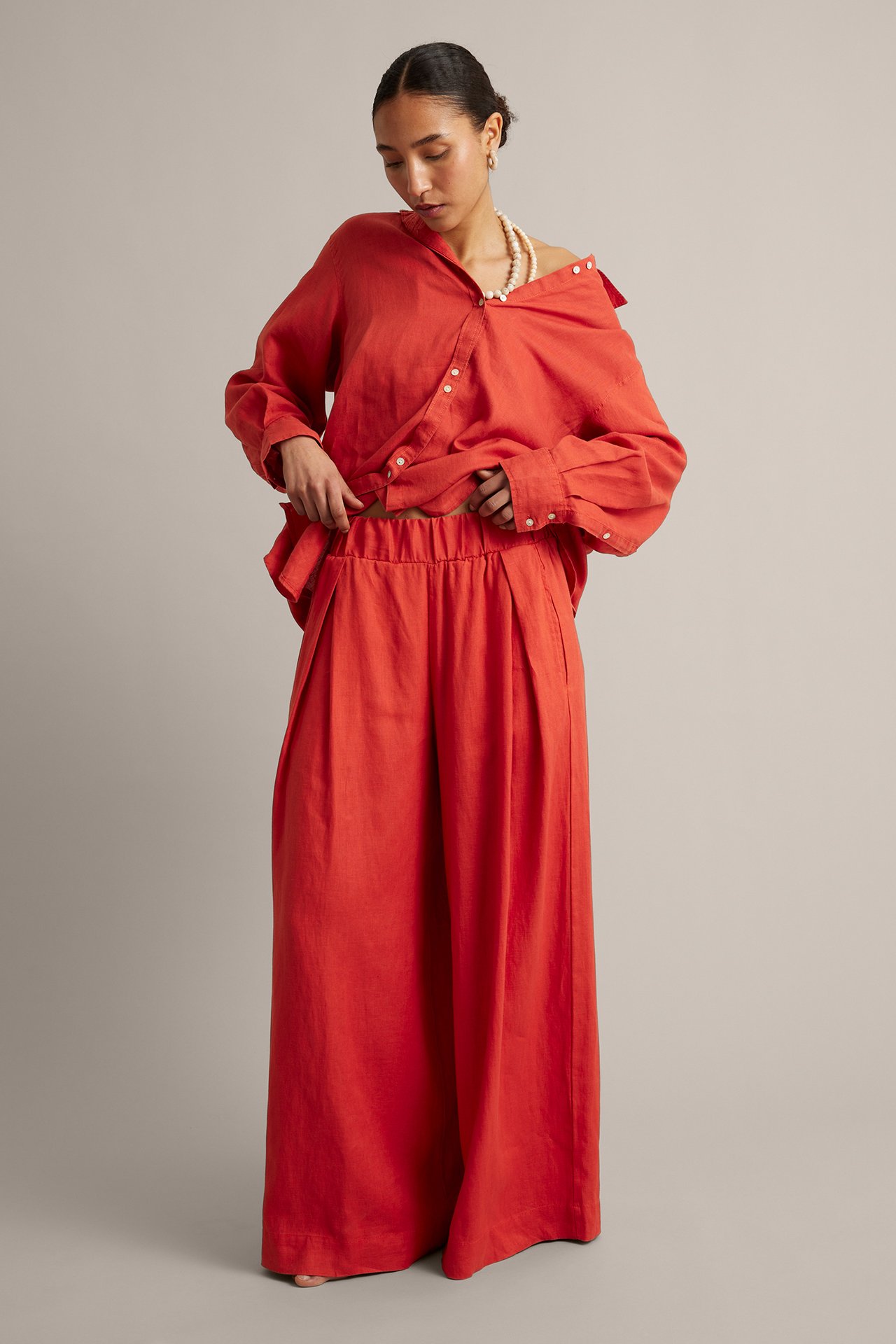 Frontvisning av kvinne i røde linbukser med vide ben, elastisk midje og matchende rød linskjorte.