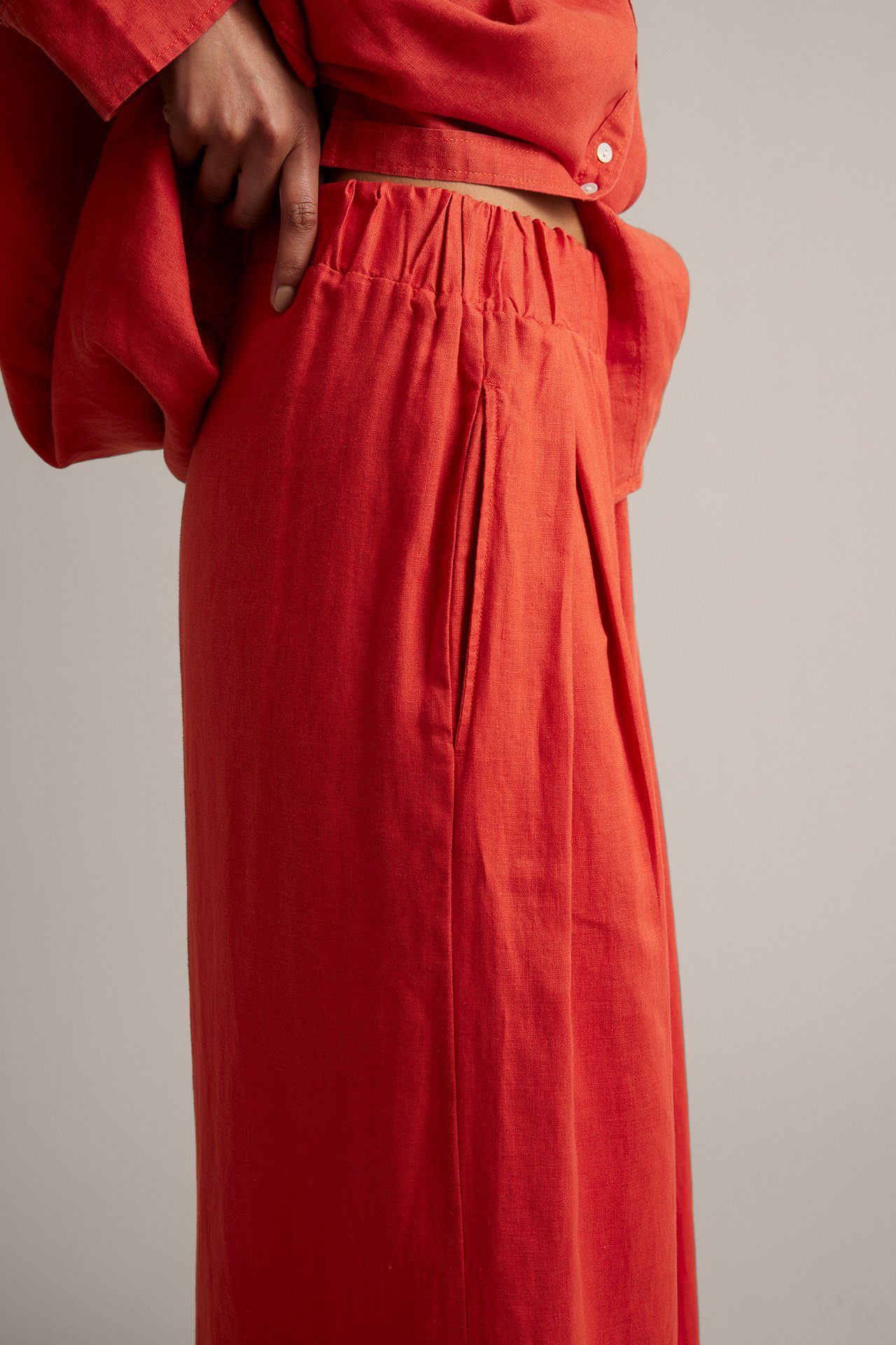 Nærbilde fra siden: Kvinne i rød vid linbukse med strikk i midjen og legg, med en rød skjorte.