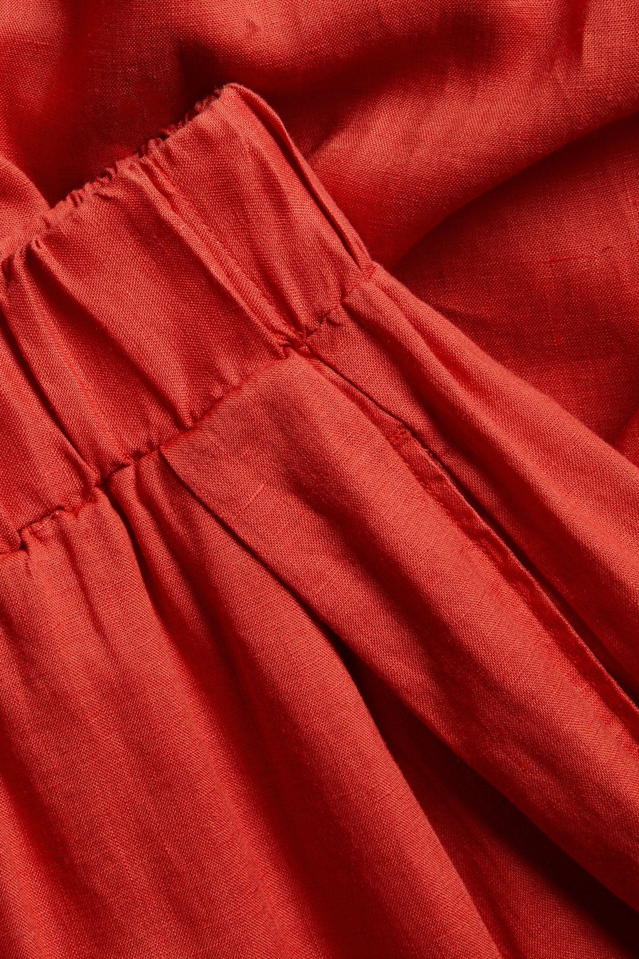 Zbliżenie na czerwone lniane spodnie wide-fit z elastyczną talią, fałdami z przodu i boczną kieszenią.