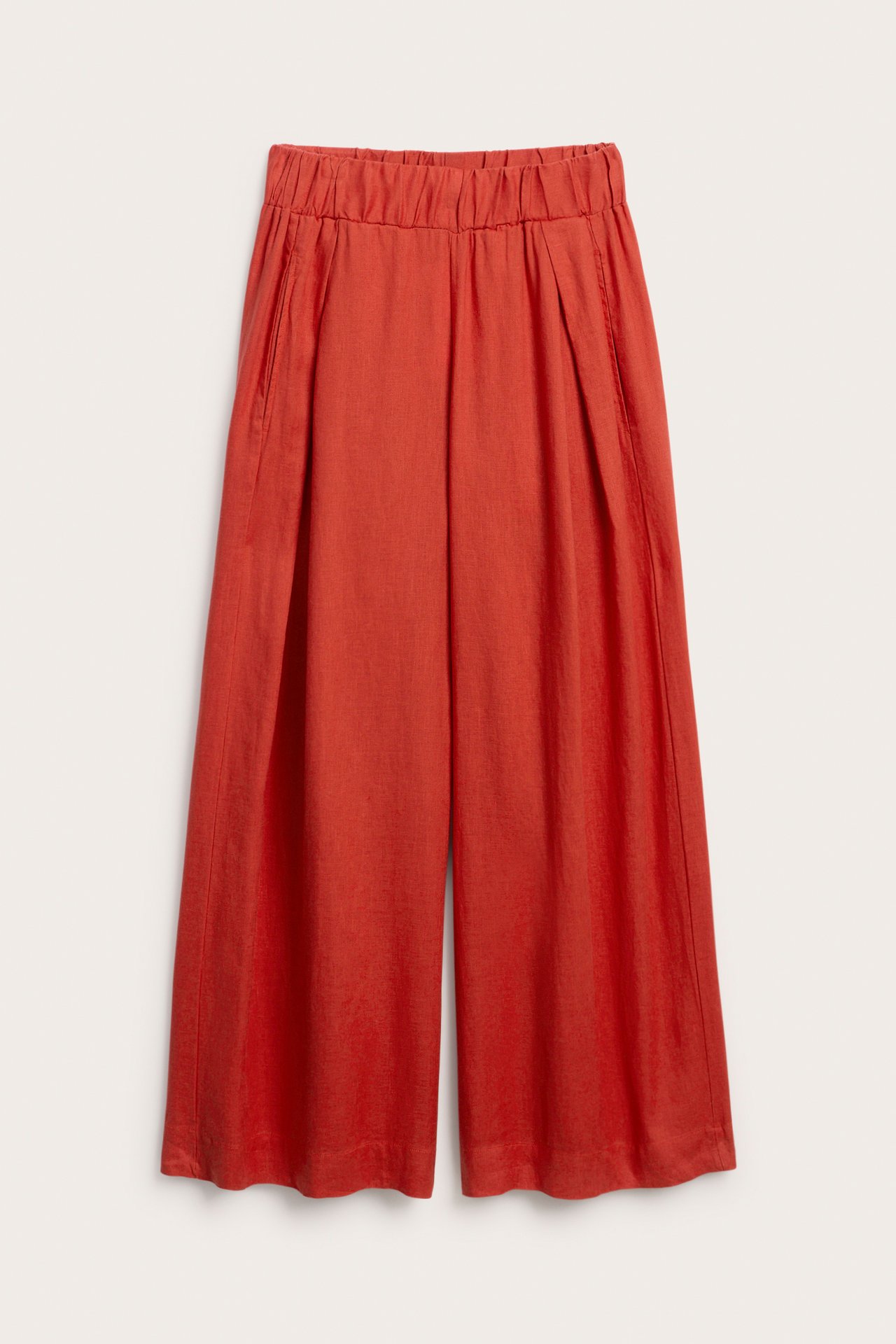 Frontvisning av røde linbukser med vide ben, elastisk linning, motfolder og sidelommer.