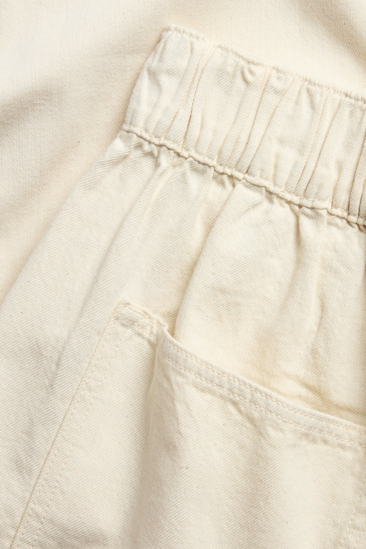 Nærbilde av lys beige bomulls-pull-on-jeans med elastisk linning og sidelomme.