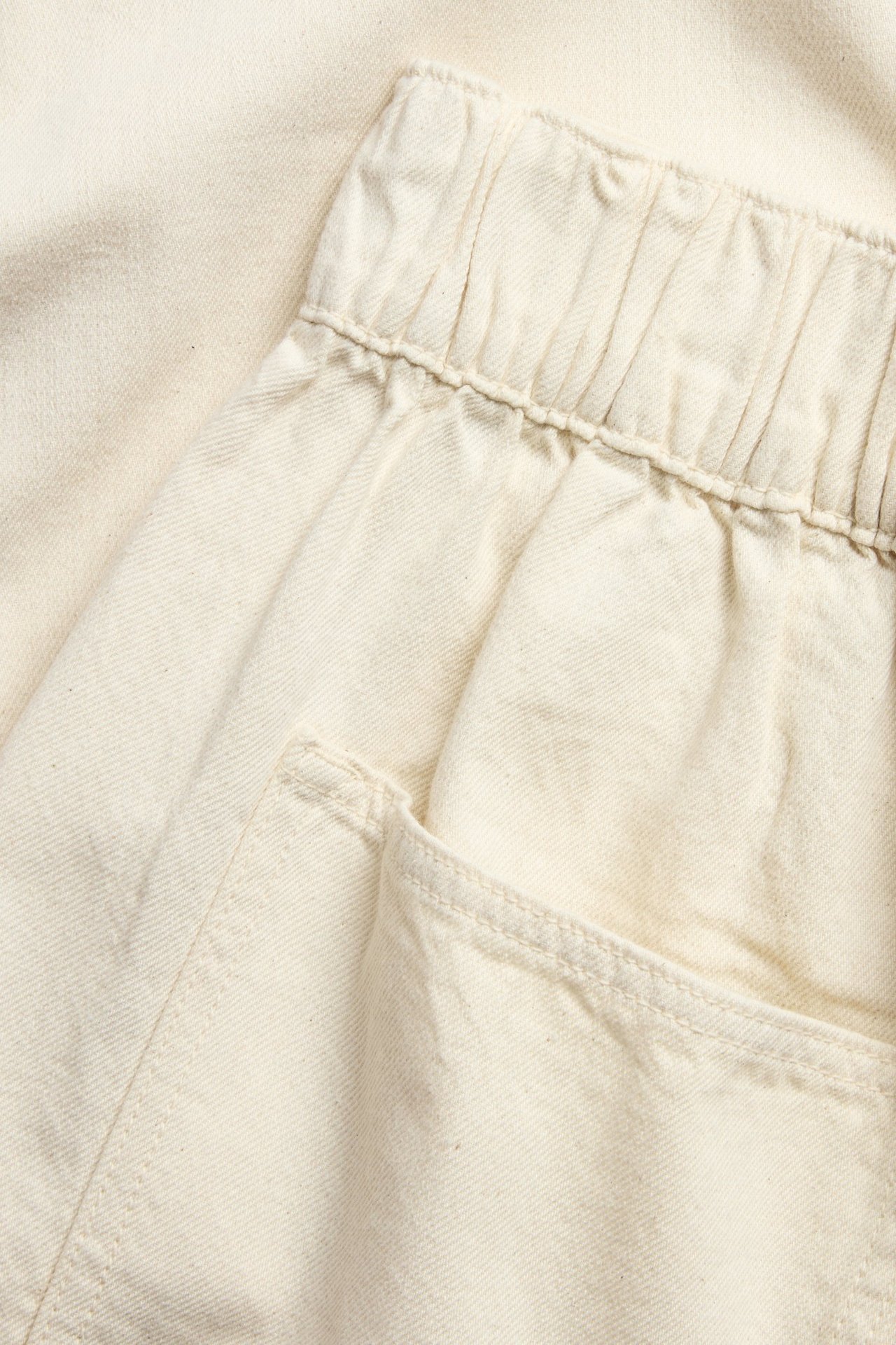 Nærbilde av lys beige bomulls-pull-on-jeans med elastisk linning og sidelomme.