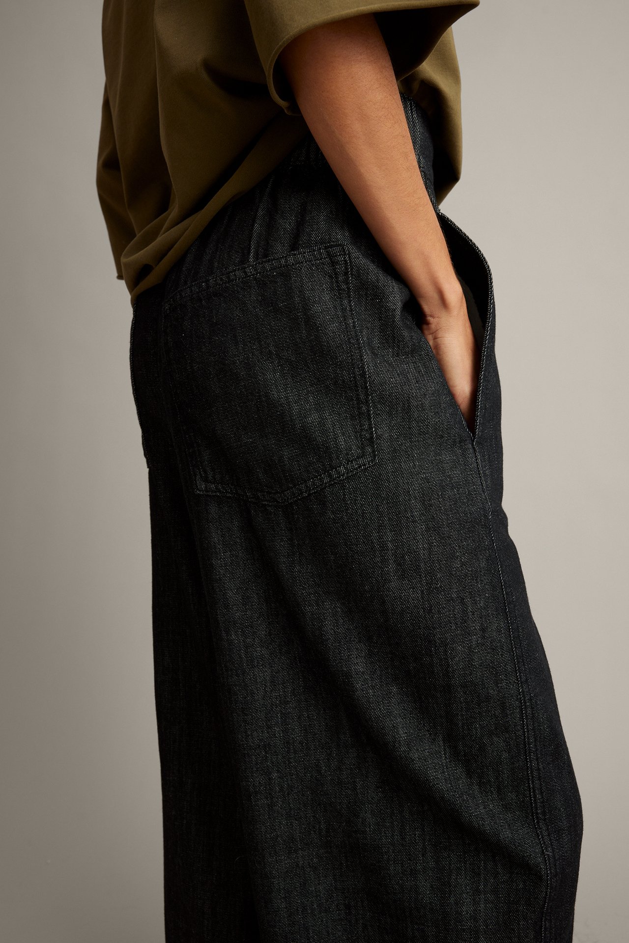 Närbild, sidovy av mörkblå lösa jeans i denim burna av kvinna med olivgrön topp.