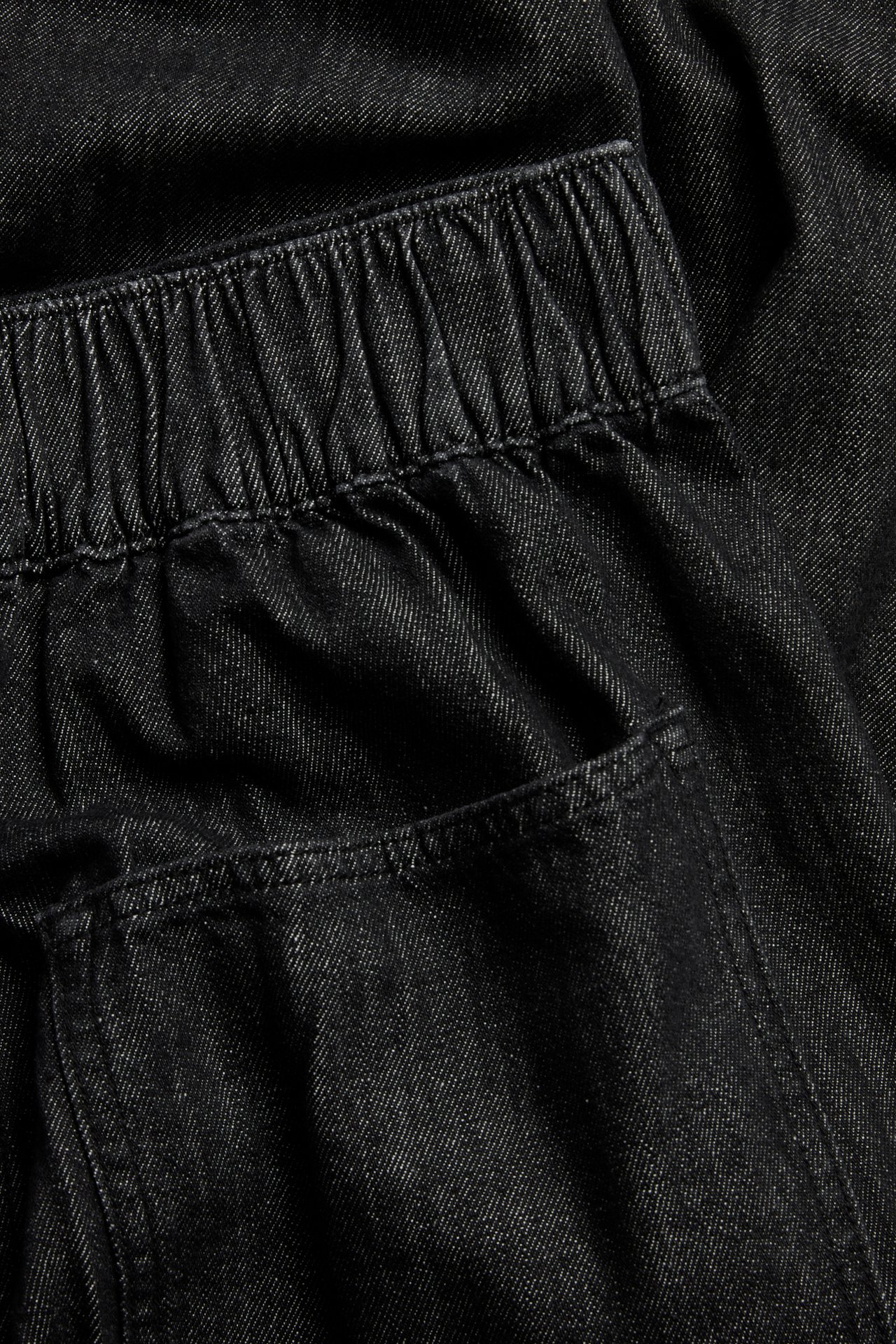 Nærbilde av svarte denim pull-on-jeans med elastisk linning og en baklomme.