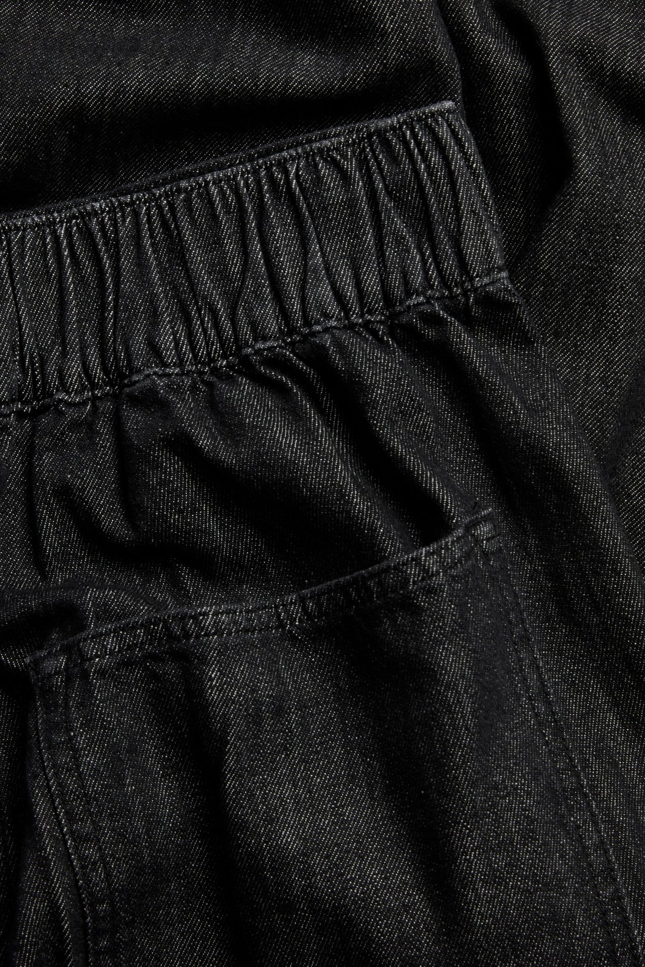 Nærbilde av svarte denim pull-on-jeans med elastisk linning og en baklomme.
