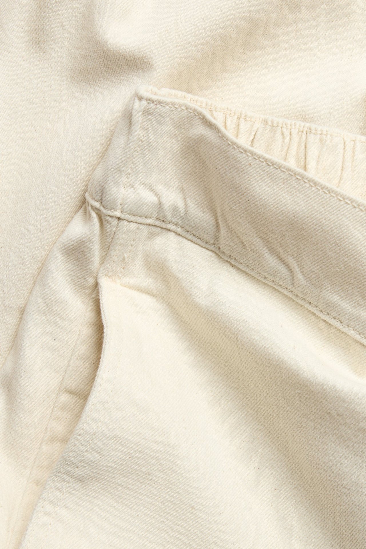 Lähikuva beigestä puuvillaisesta suoralahkeisesta farkusta, jossa resori vyötäröllä ja tasku.