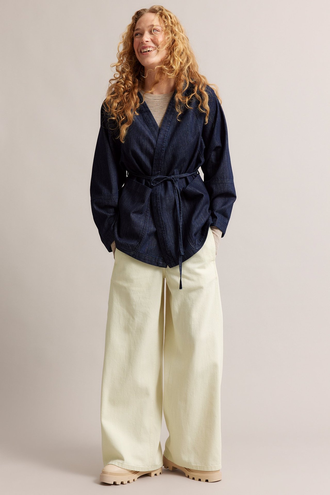 Edestä, nainen yllään beiget leveälahkeiset pull-on farkut, tummansininen sidottava farkkutakki ja vaaleanbeiget kengät.