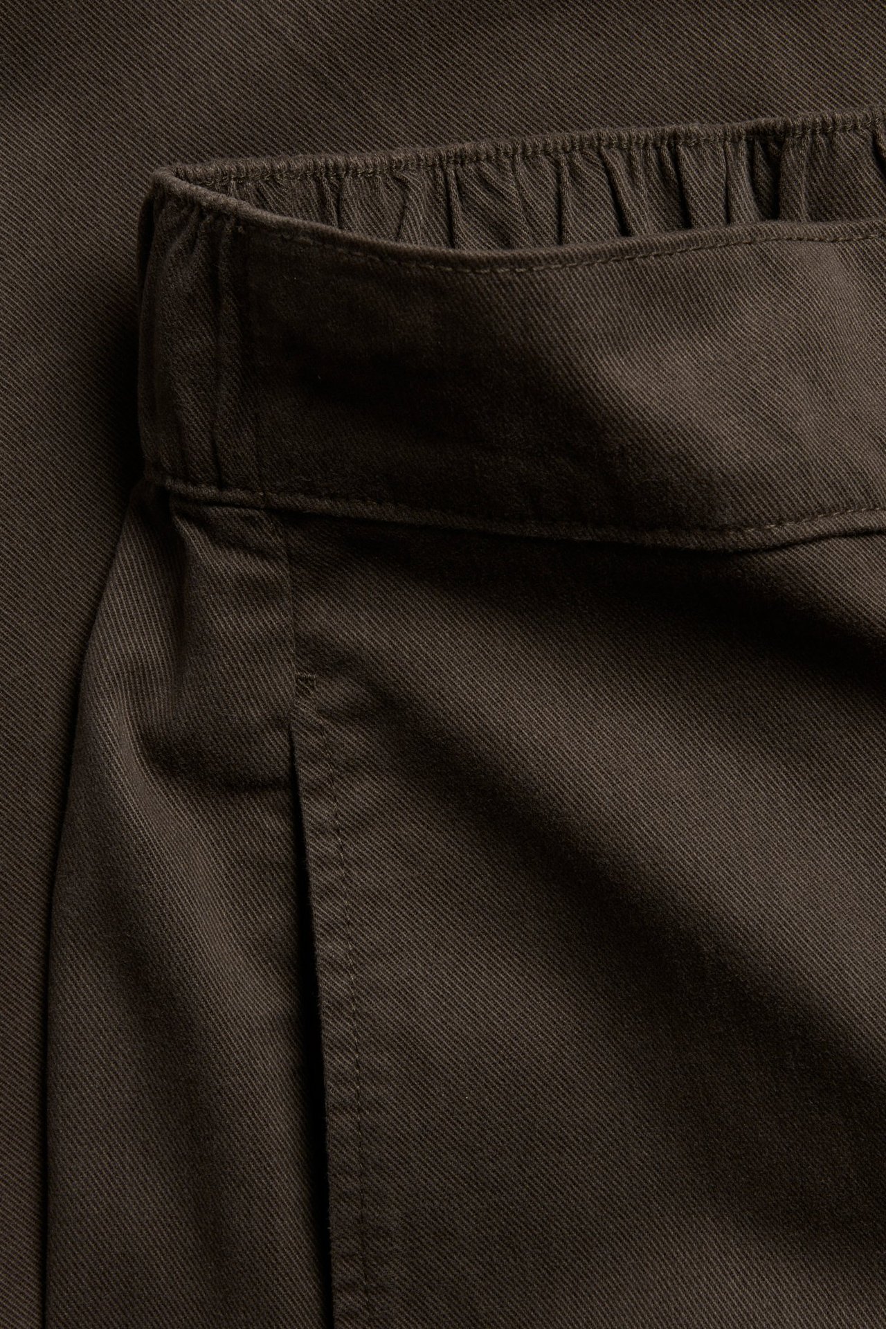 Zbliżenie brązowych spodni pull-on z bawełny i lyocellu z elastycznym pasem oraz detalami szwów bocznych.