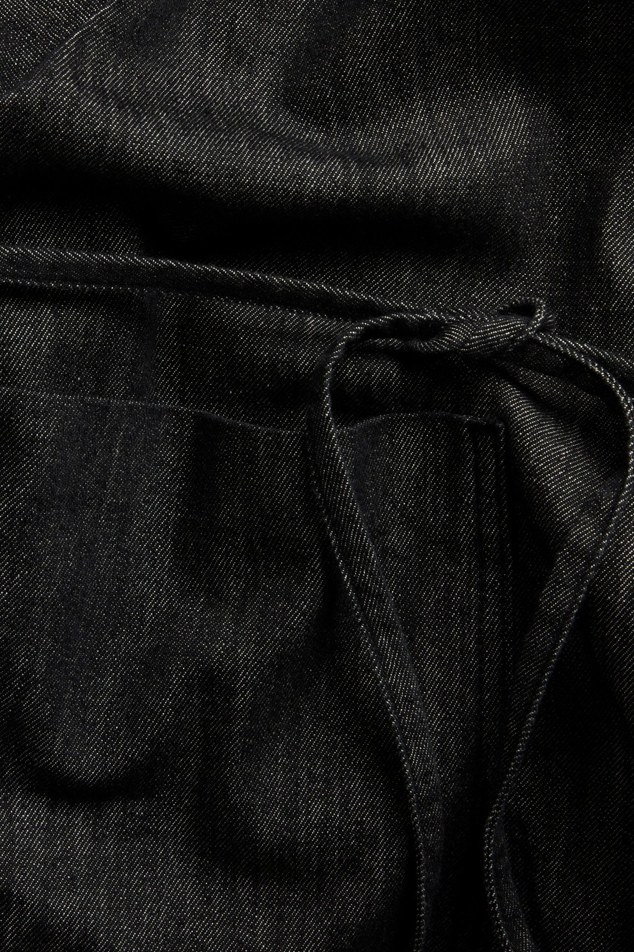 Zbliżenie czarnej kurtki kimono z denimu z wiązanym paskiem i dużą przednią kieszenią.