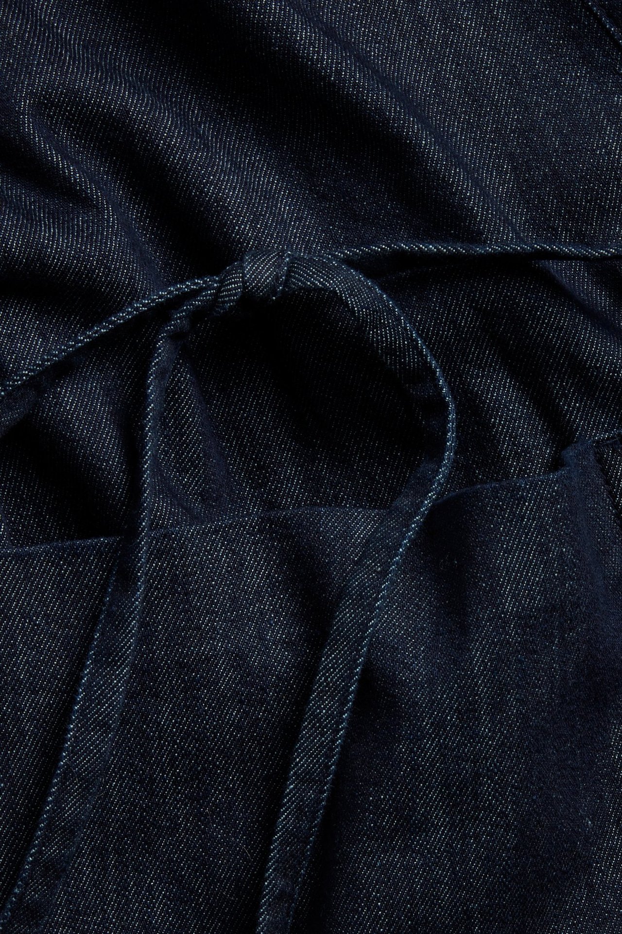 Zbliżenie na ciemnoniebieską kurtkę jeansową kimono z wiązanym paskiem.