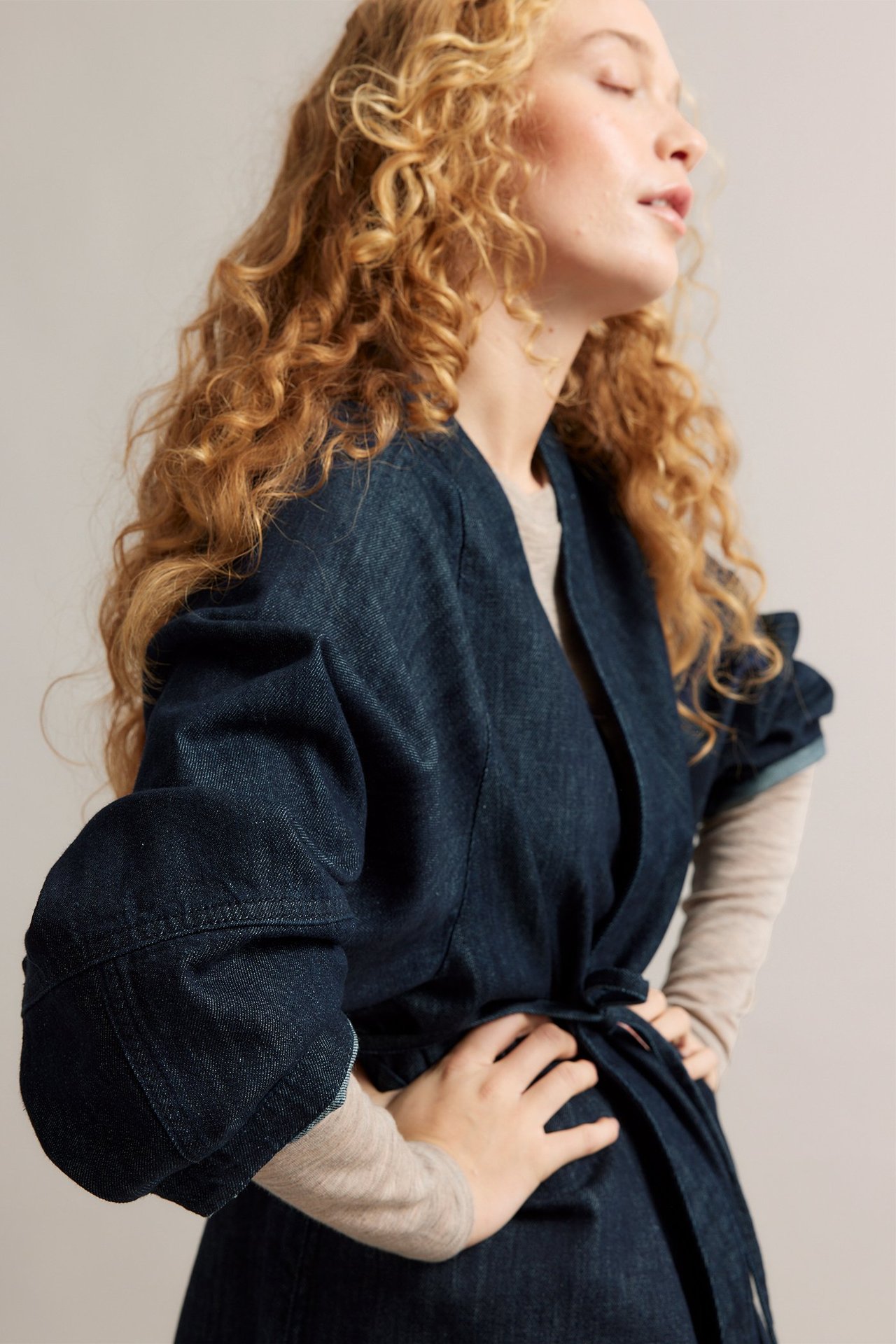 Boczny widok kobiety w ciemnej dżinsowej kurtce kimono z wiązanym paskiem na jasnobeżowym topie.