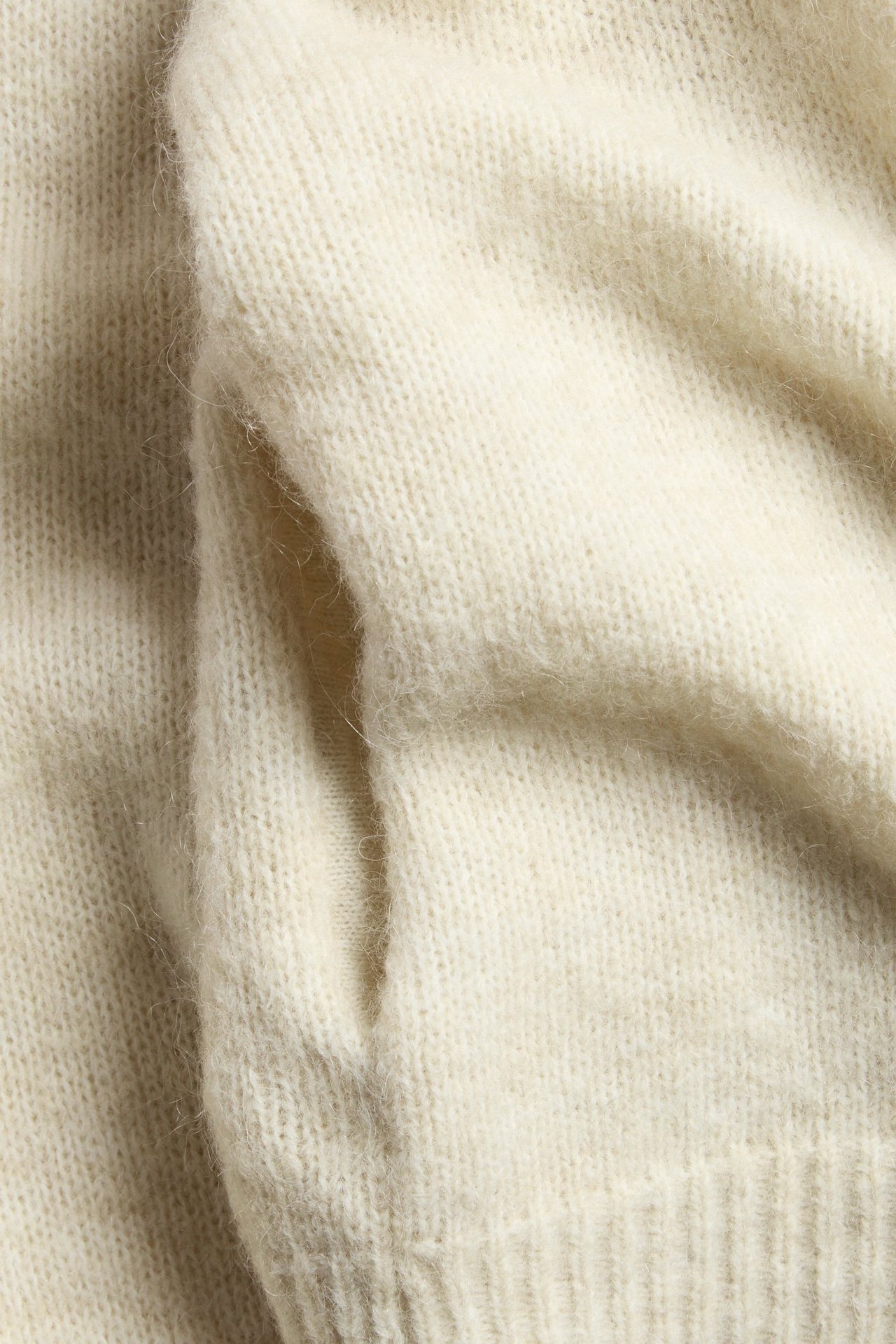 Lähikuva vaaleanbeigestä villasekoite-neuletakista, näyttäen sen pehmeän neulotun pinnan ja sivutaskun.