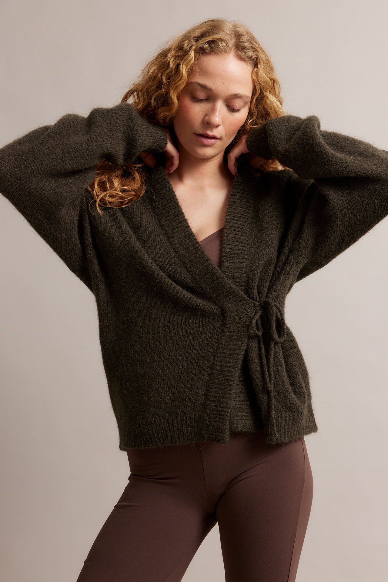 Frontbilde: Kvinne i mørkbrun ullblanding-knytecardigan, lysbrun camisole og mørkebrune leggings.