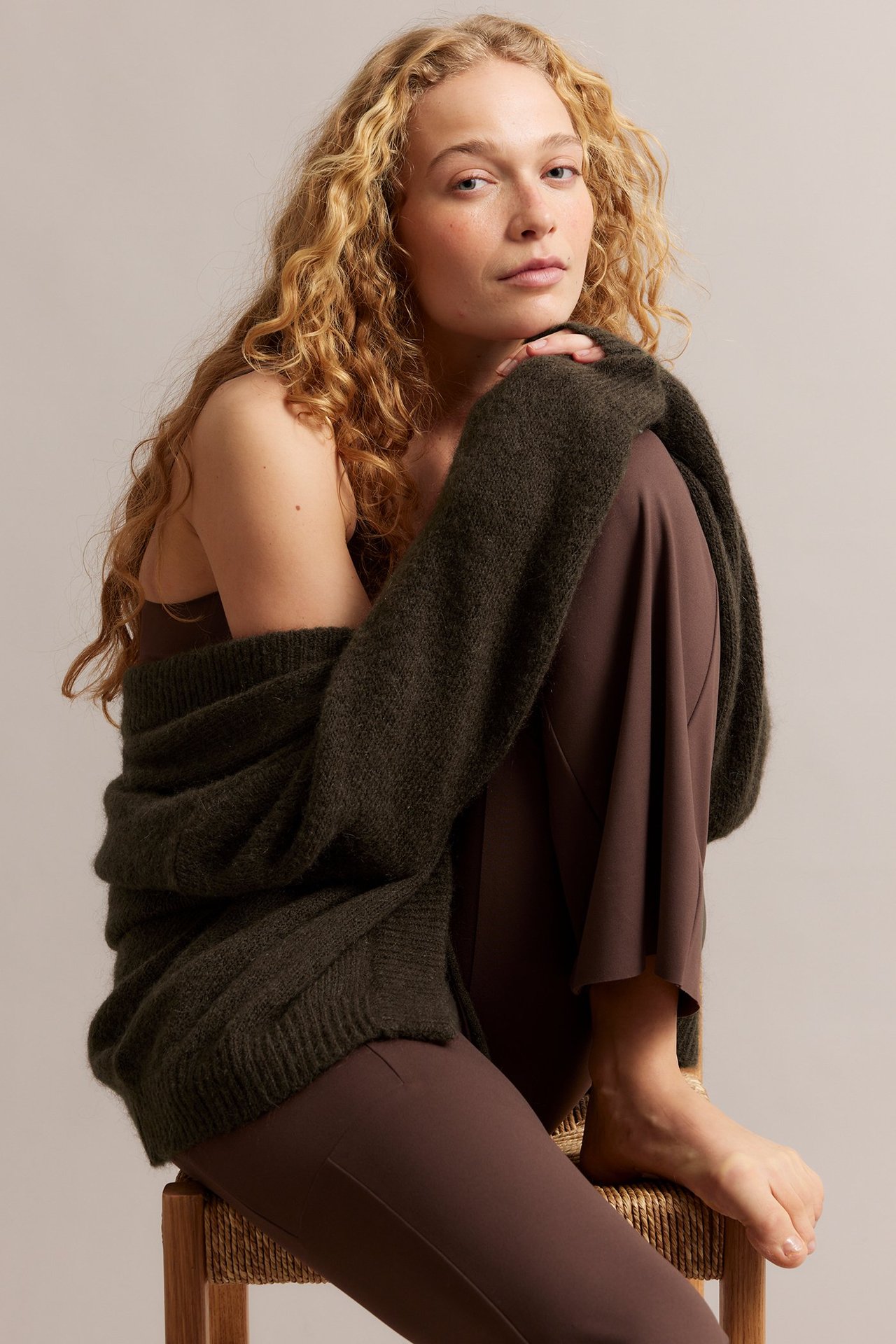 Edestä: Nainen yllään tummanruskea villasekoitekardigaani ruskean topin ja leveälahkeisten housujen päällä.