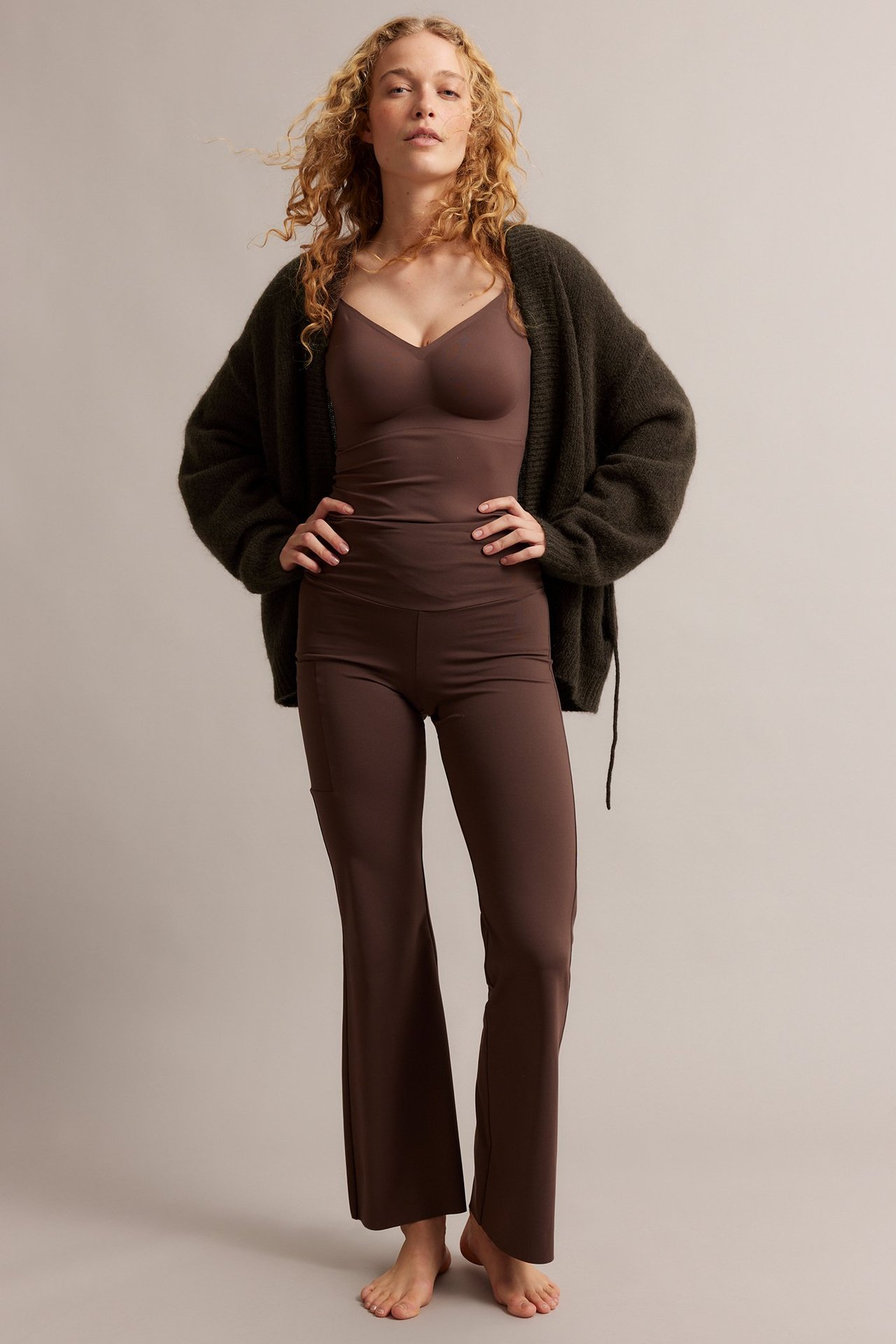 Kvinne i åpen, mørk brun ullblanding-cardigan med knytebånd, over matchende brun camisole og bukser.