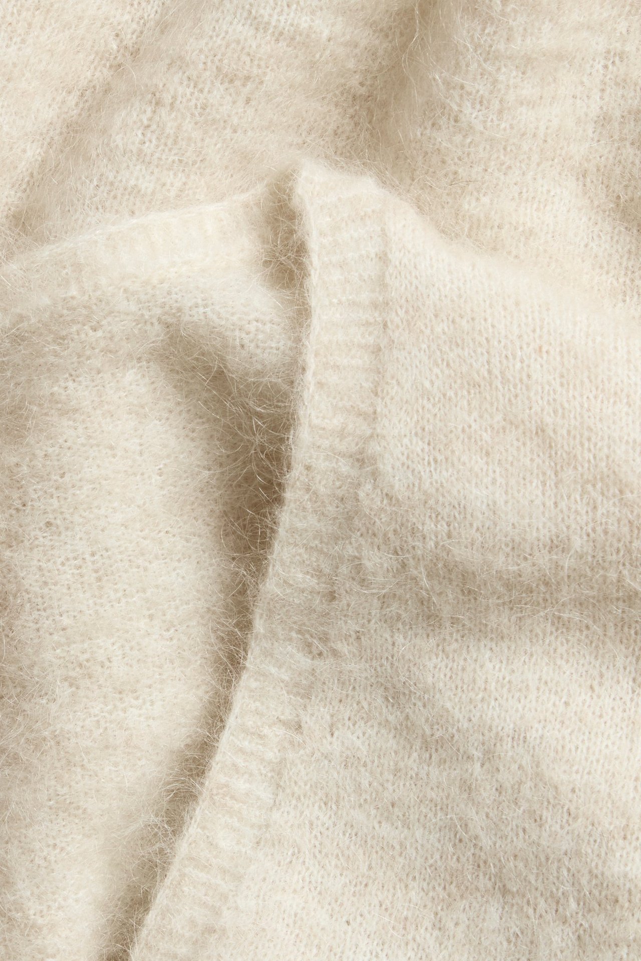 Zbliżenie jasnobeżowego, puszystego materiału kardiganu kopertowego z mieszanki wełny.