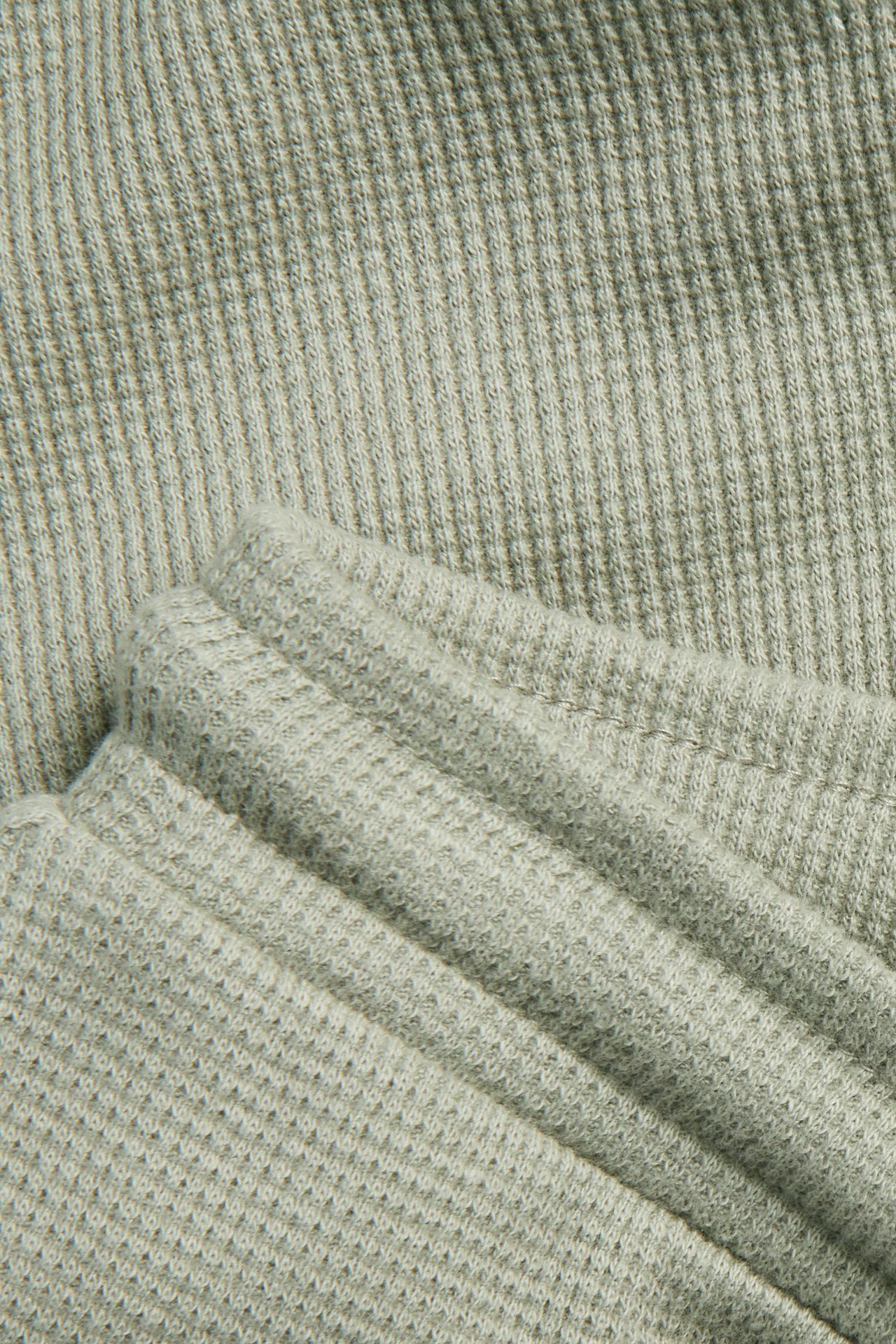 Zbliżenie na ciemnozielone bawełniane spodnie o splocie waflowym, pokazujące fakturę i zagniecenia.