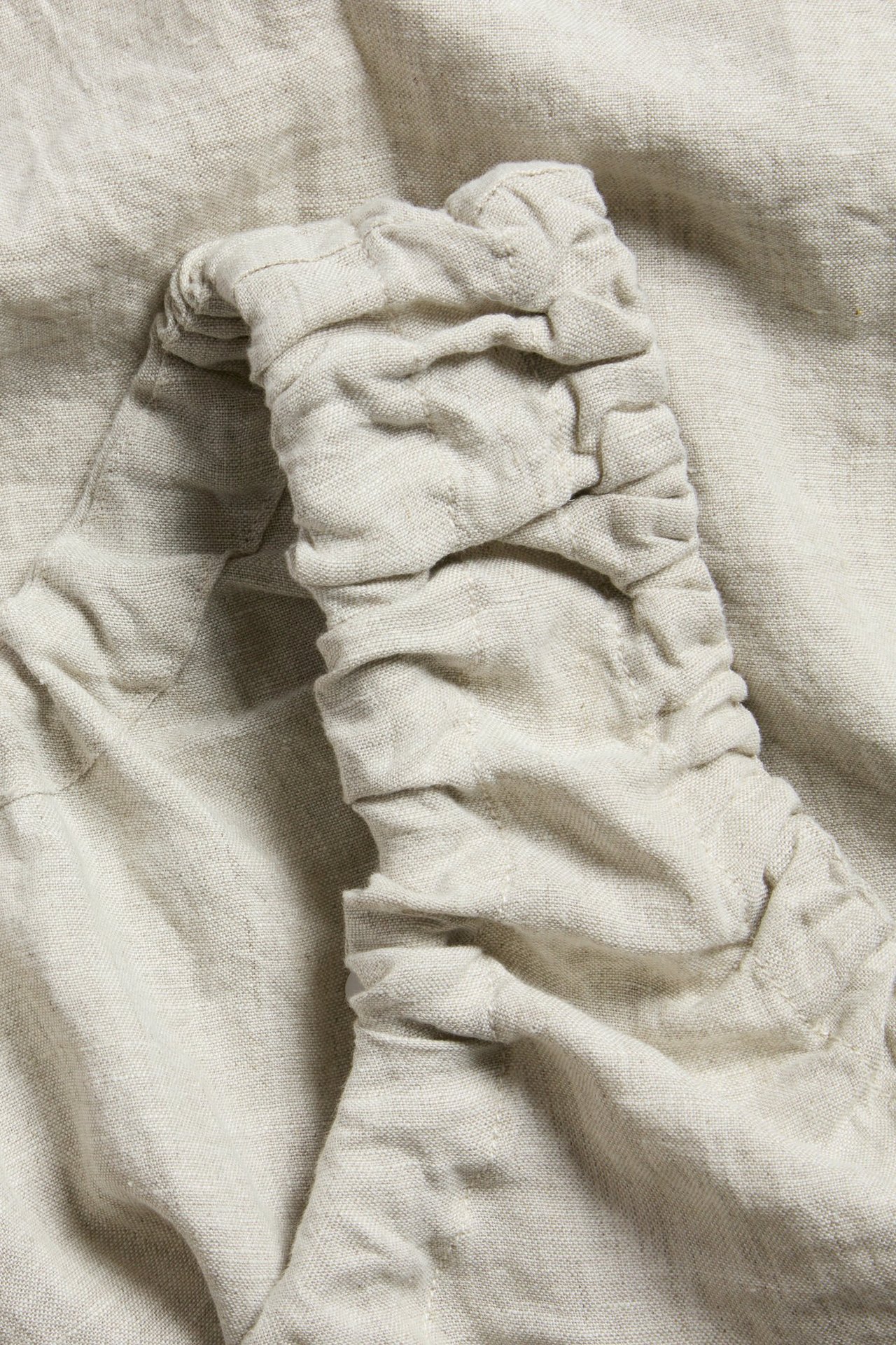 Zbliżenie beżowego lnianego topu ukazujące marszczone detale i szwy ze sznurkowego dekoltu.