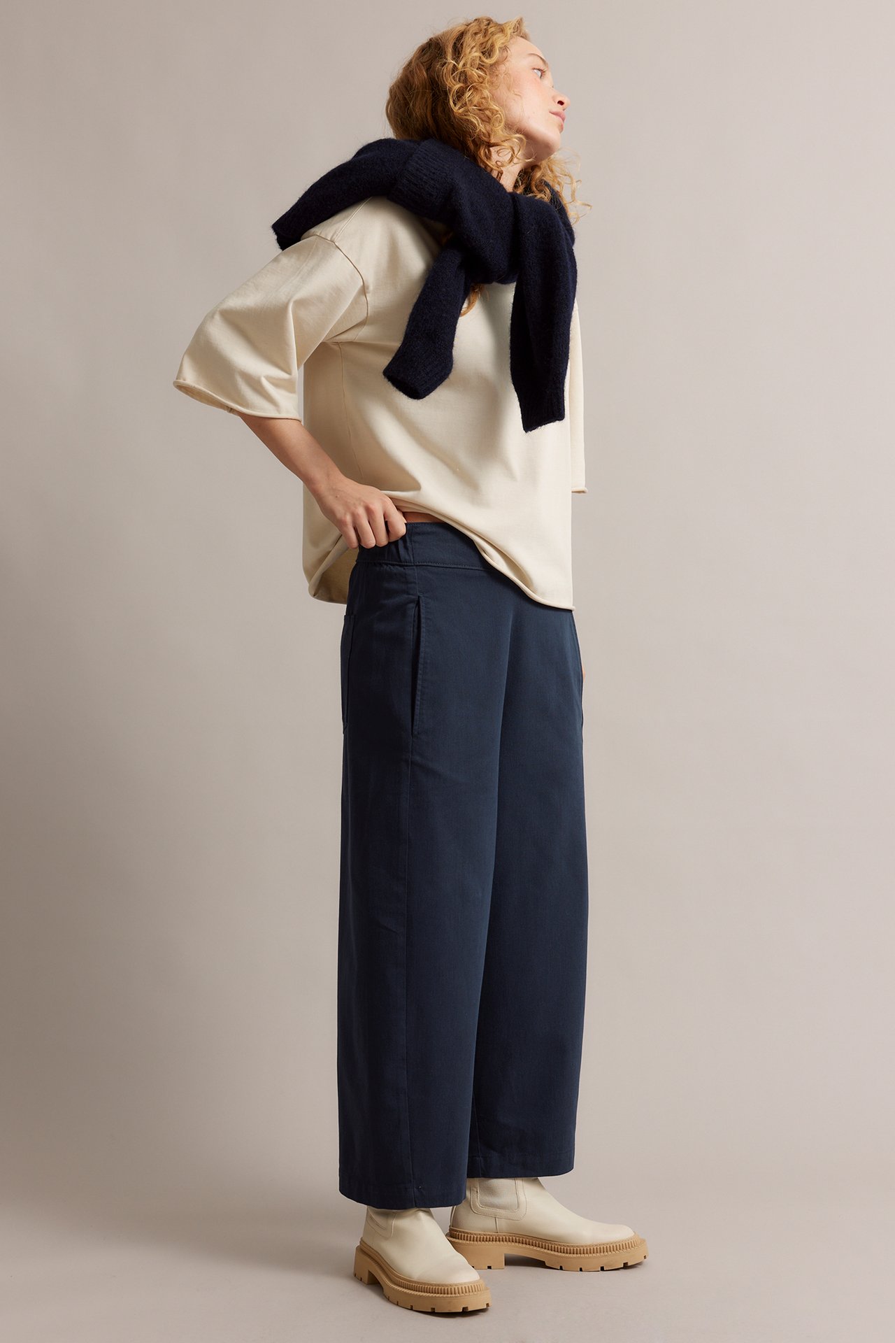 Sivukuva: Nainen sinisissä leveissä pull-on-housuissa, beigessä t-paidassa, tummansinisessä neuleessa, kermakengissä.