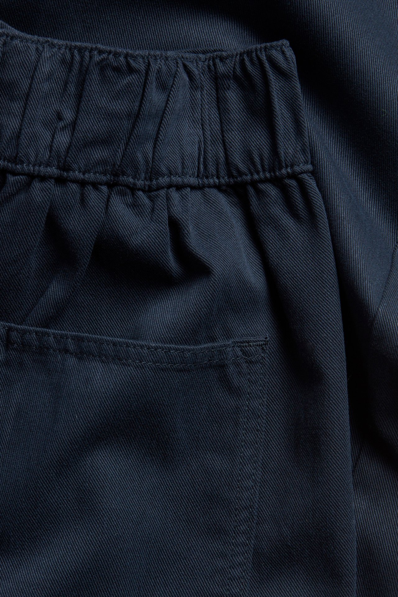 Zbliżenie ciemnoniebieskich spodni pull-on z elastycznym pasem i tylną kieszenią z bawełny i lyocellu.