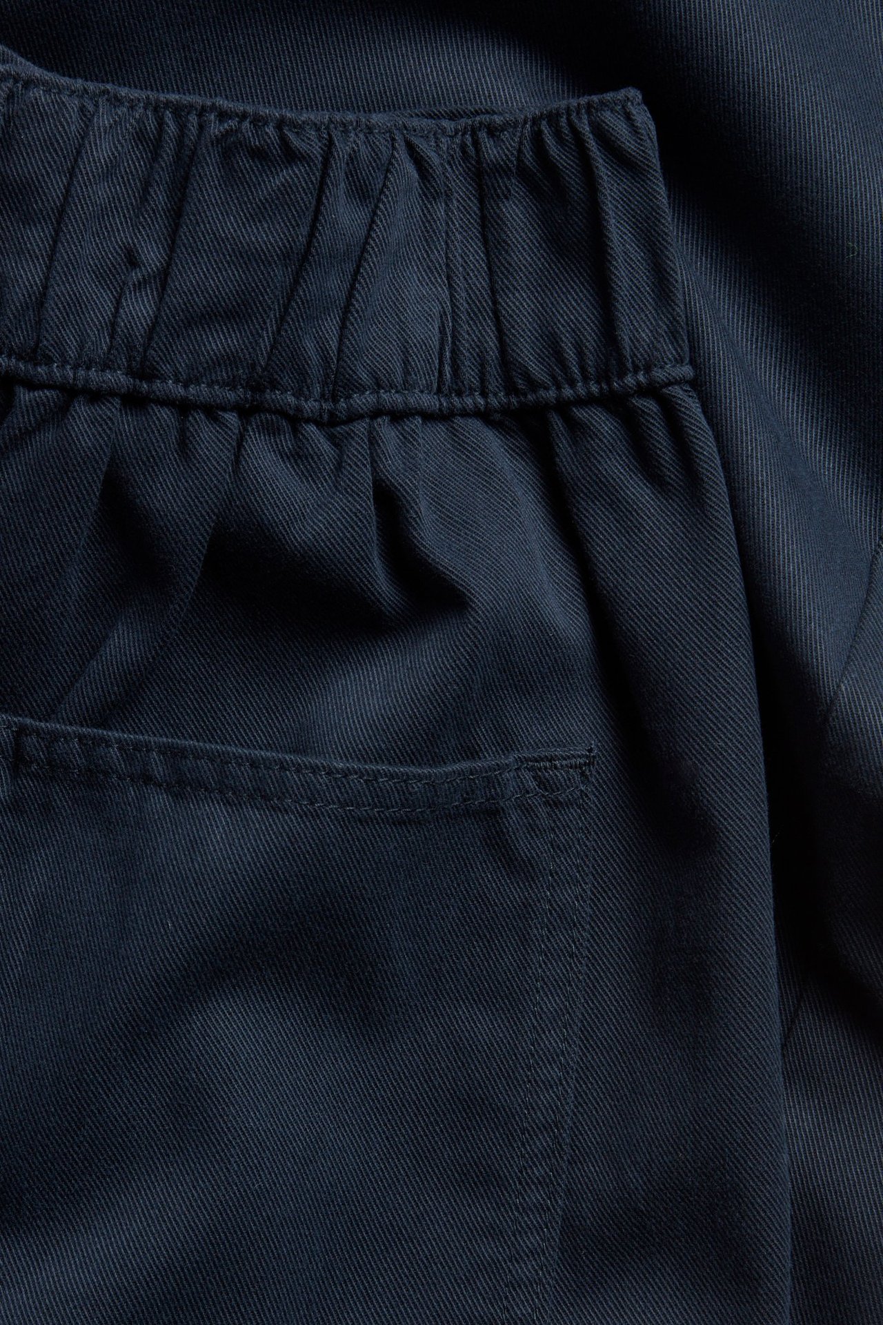 Zbliżenie ciemnoniebieskich spodni pull-on z elastycznym pasem i tylną kieszenią z bawełny i lyocellu.