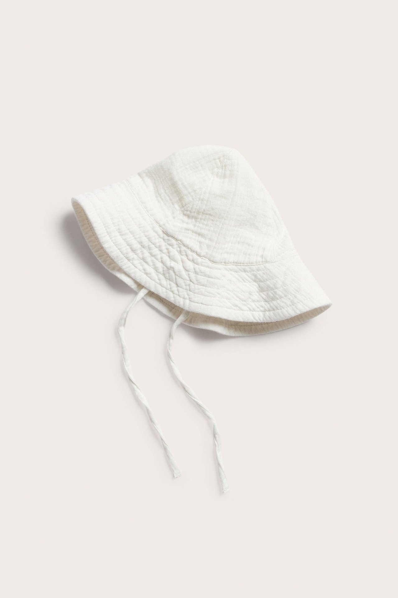 Offwhite baby bomullssolhatt med knytband, texturerad yta, vy uppifrån.