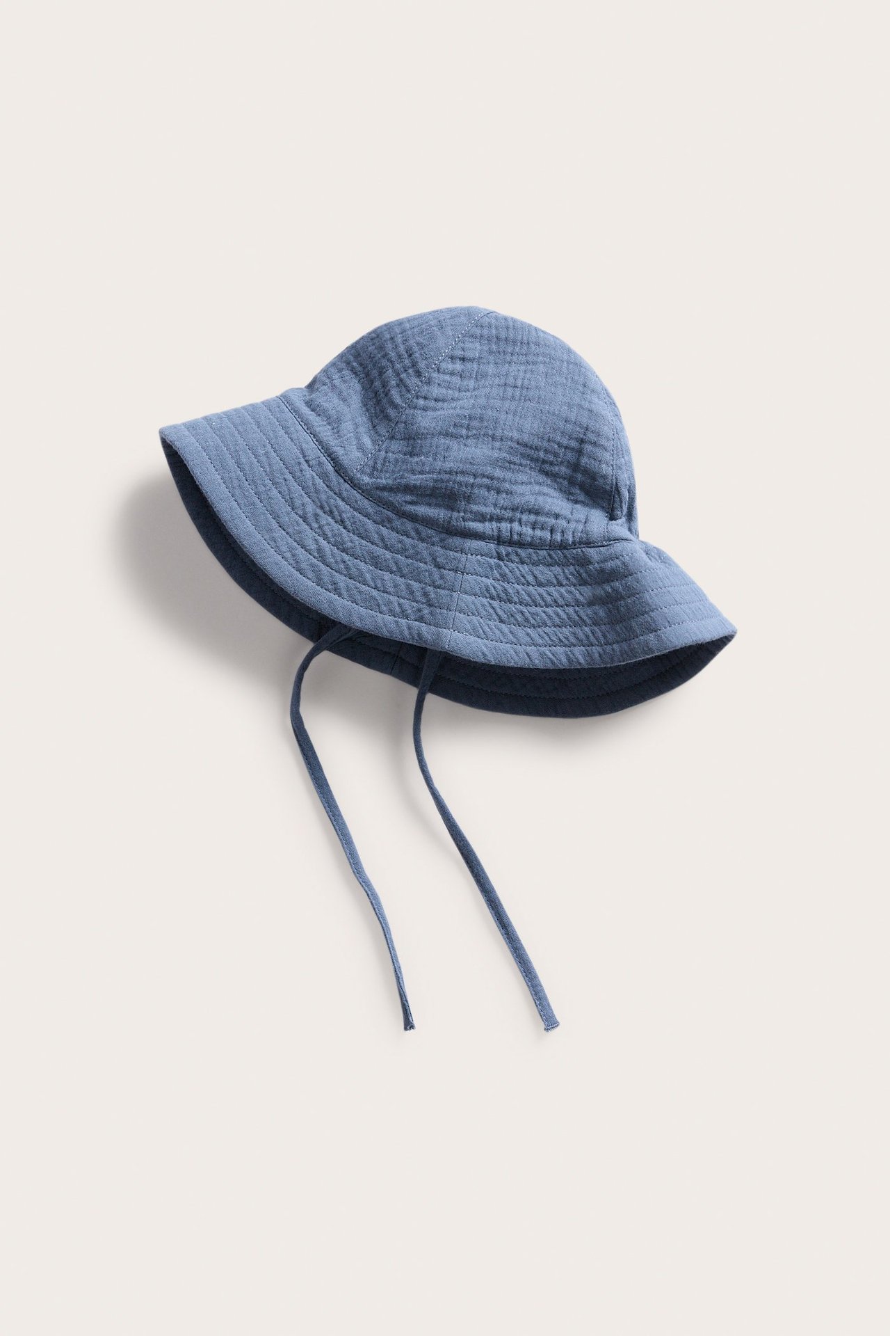 Sidovy av en blå krinklad solhatt i bomull med knytband för baby.