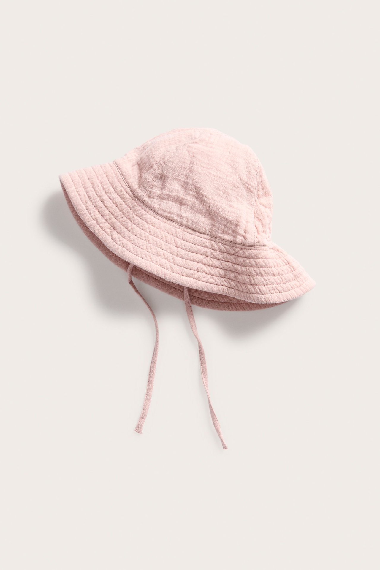 Framsida av en enfärgad rosa solhatt i bomull för baby med bred brätte och knytband.