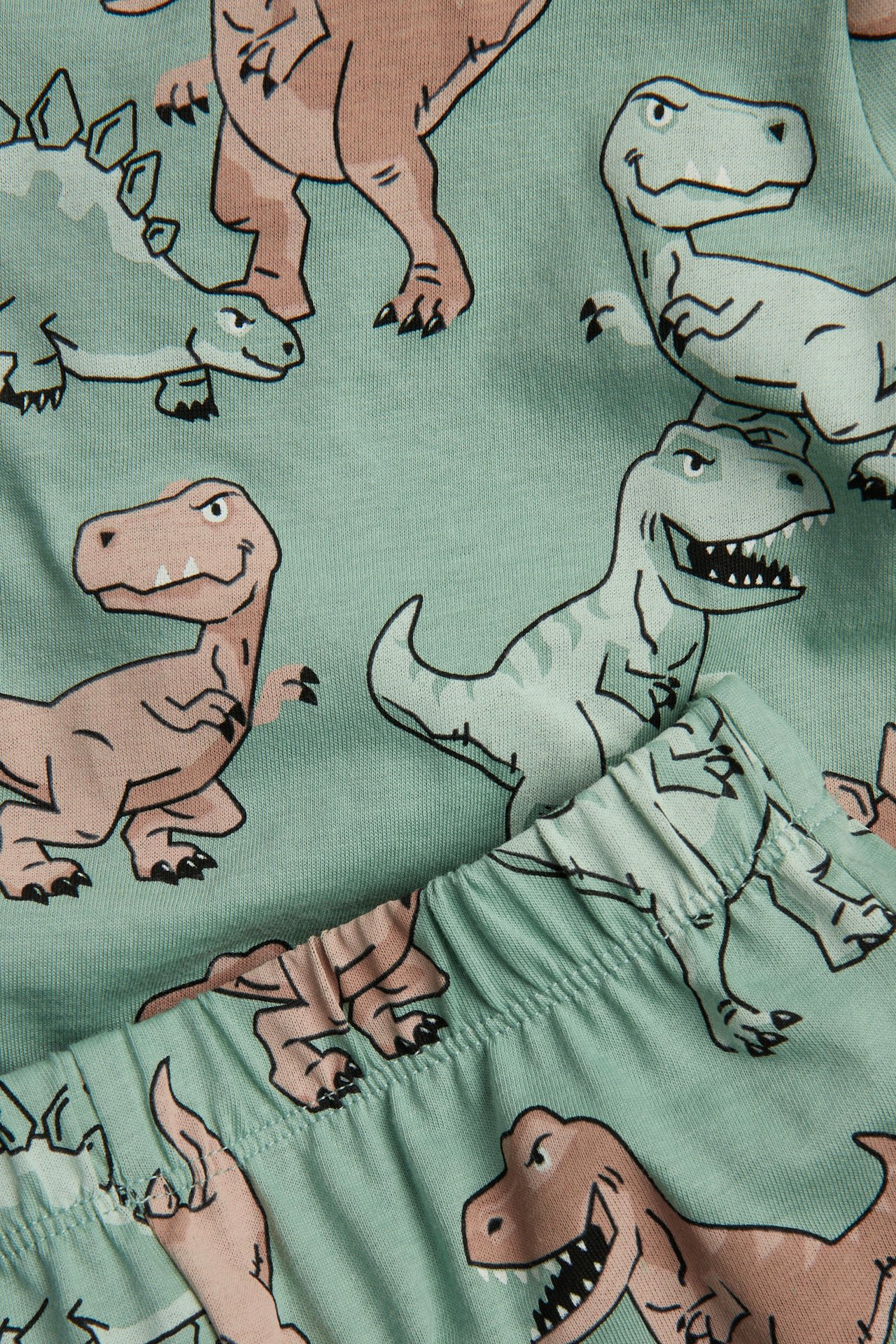 Närbild på en barns grön bomullspyjamas med heltäckande dinosauriemönster och resårmidja.