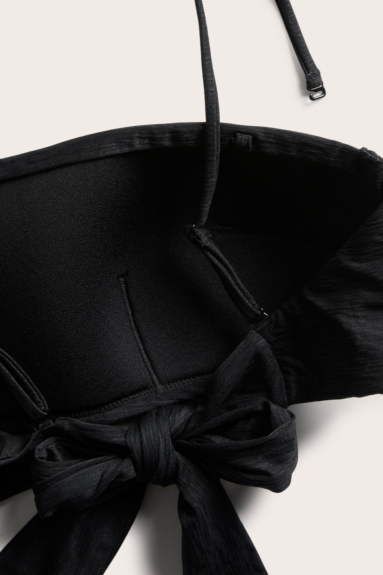 Lähikuva mustasta kuvioidusta topatusta bandeau-bikiniyläosasta irrotettavilla olkaimilla, edessä rusetti.