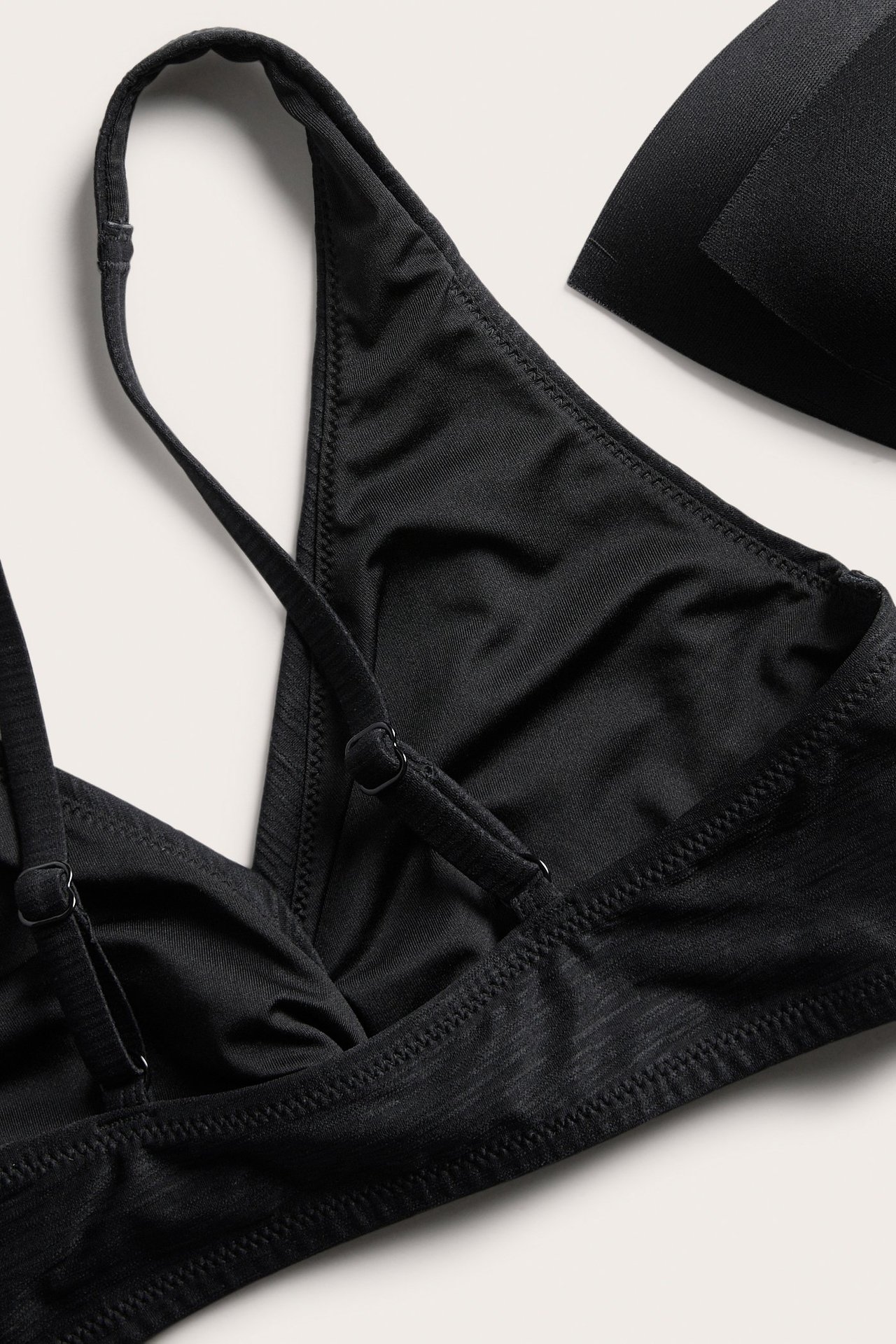 Lähikuva: musta strukturoitu bikinitoppi kierretyllä etuosalla, säädettävillä olkaimilla ja irrotettavalla toppauksella.