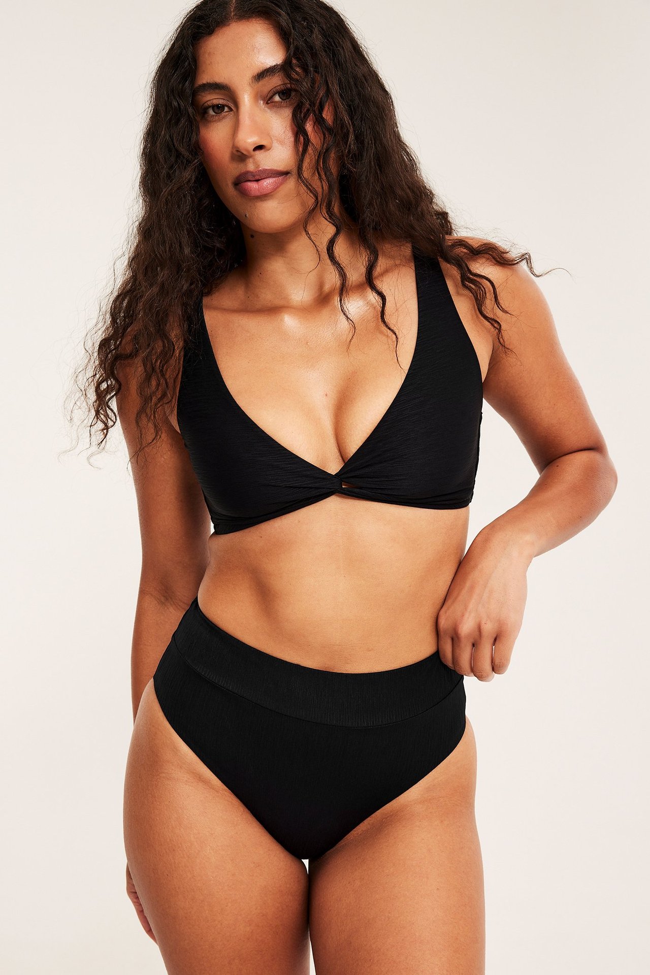 Forfra, kvinne i svart strukturert brazilian high-leg bikinitruse og matchende strukturert bikinitopp.