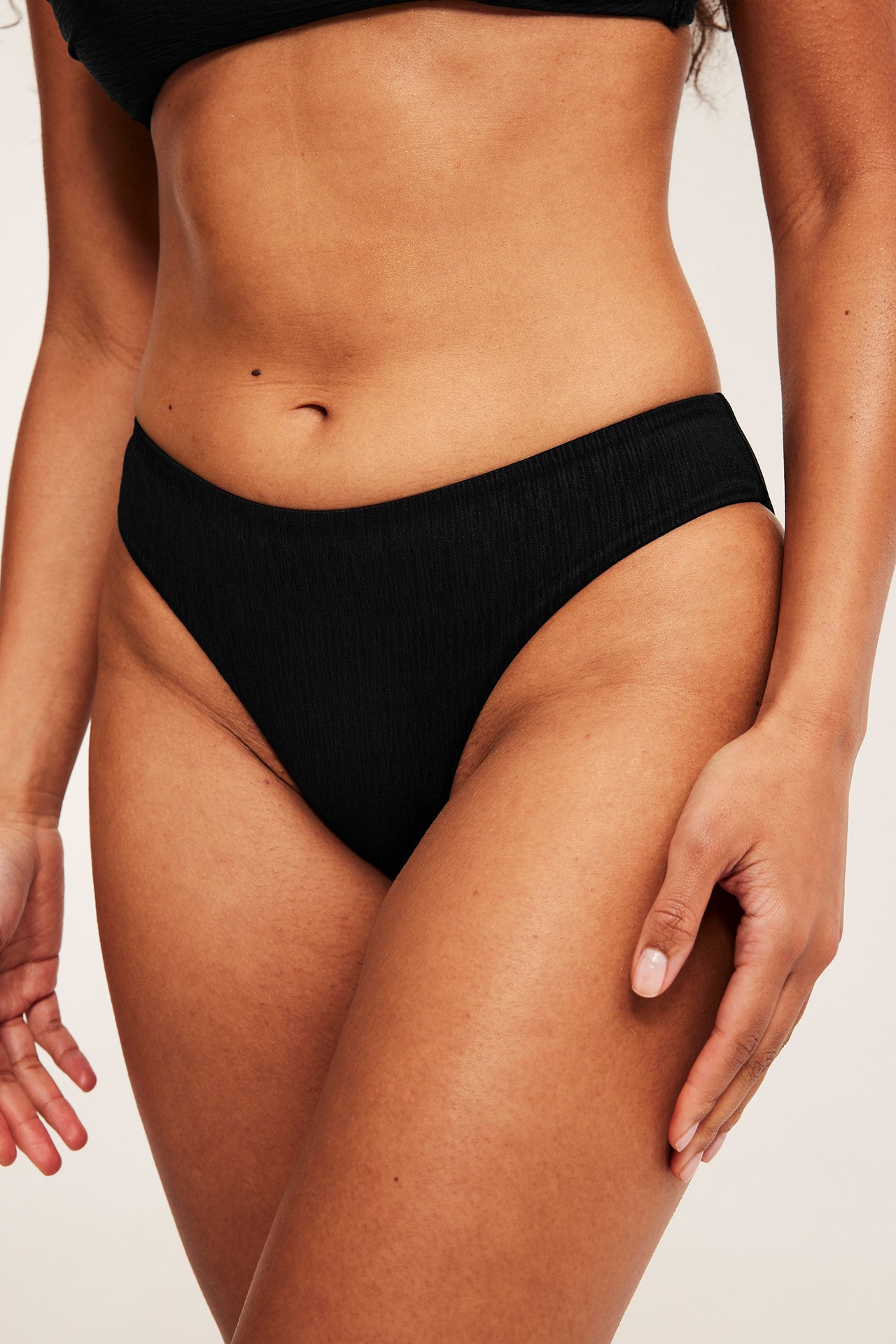 Nærbilde forfra av en kvinne i sort strukturert bikinitruse og matchende bikinitopp.