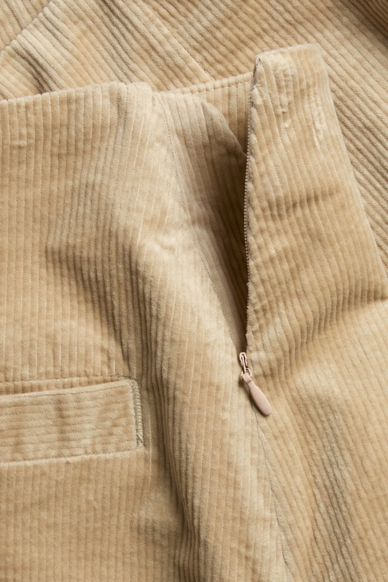 Zbliżenie na beżową krótką spódnicę sztruksową z bocznym zamkiem i przednią kieszenią.