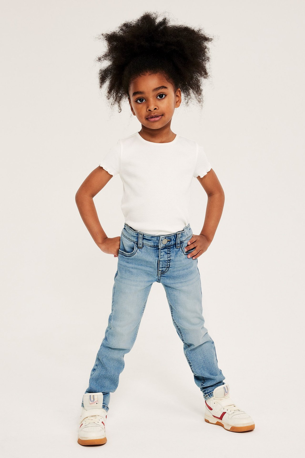 Edestä, lapsi vaaleansinisissä slim-farkuissa, valkoisessa ribbi-t-paidassa ja valkoisissa tennareissa.