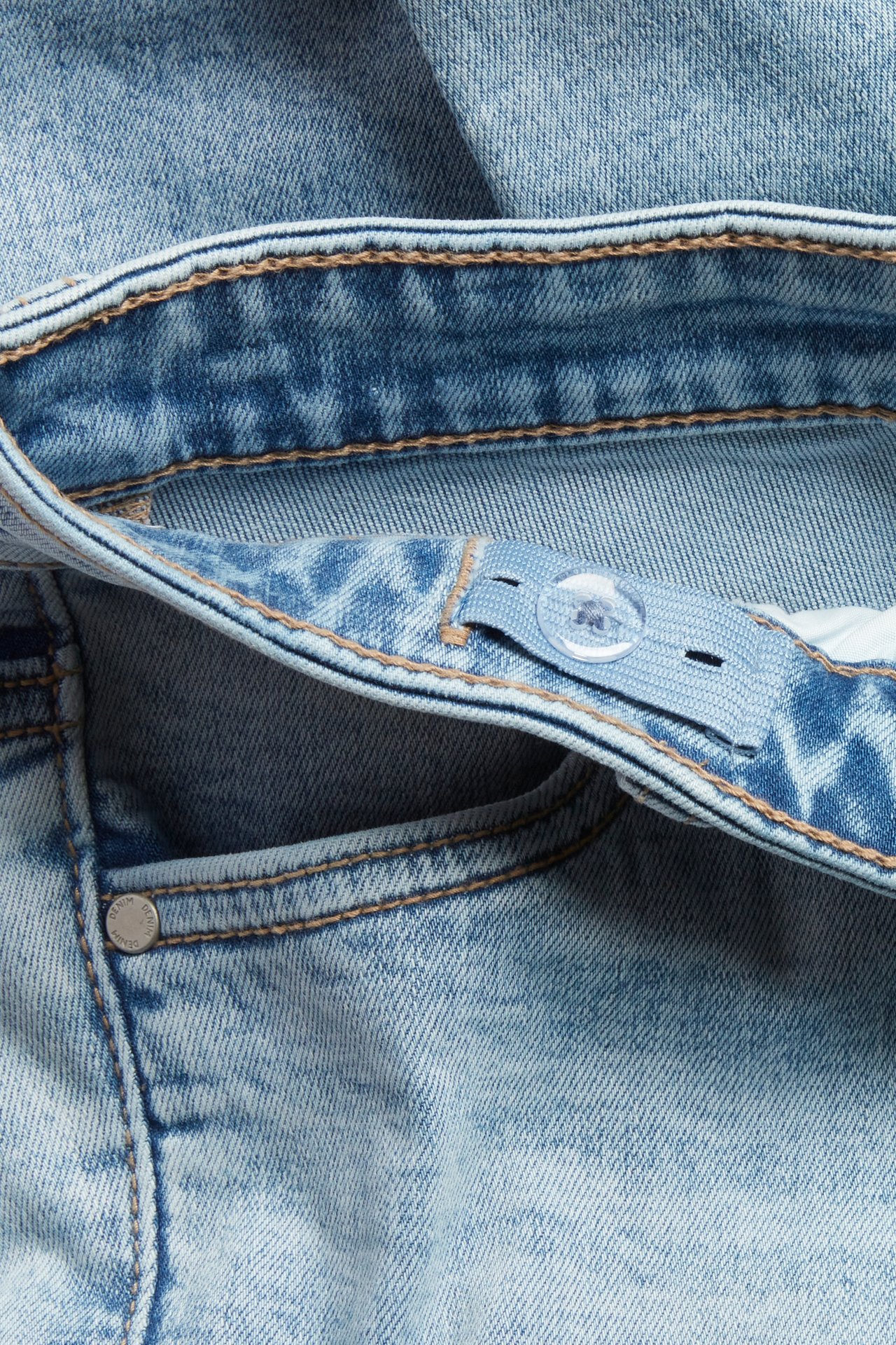 Närbild på barnslimjeans i ljus denim med justerbar midja, resår, klar knapp och metallnit.