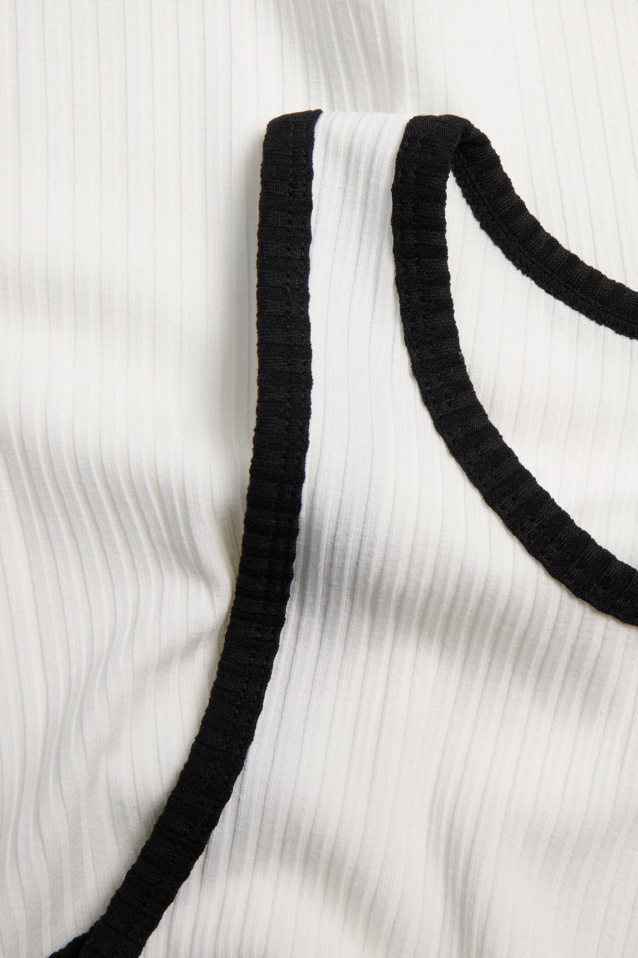 Nærbilde av en offwhite ribbet topp med svarte kontrastkanter.