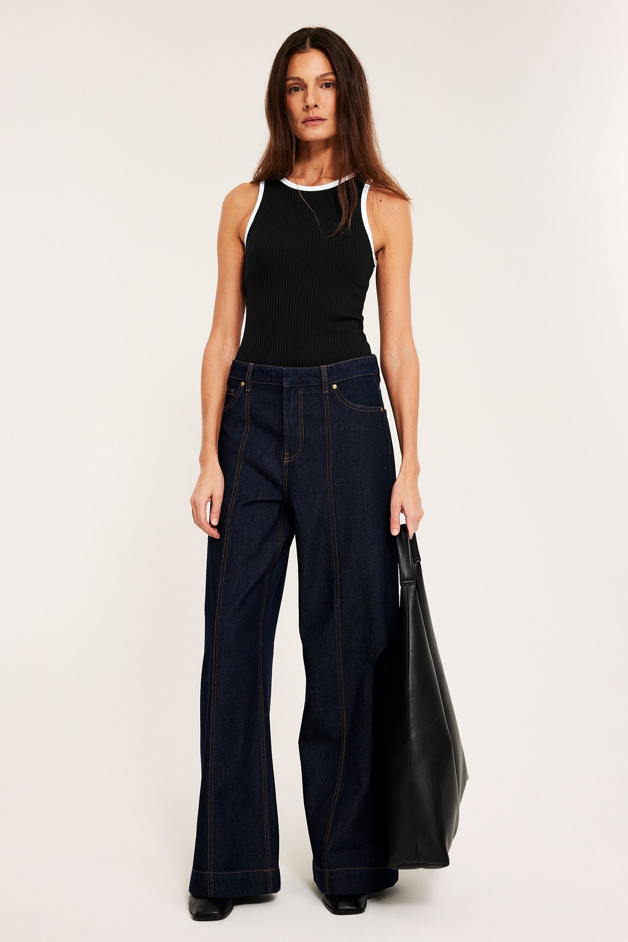 Frontbilde: Kvinne i svart ribbet singlet med hvite kanter, mørkeblå vide jeans, med svart totebag.