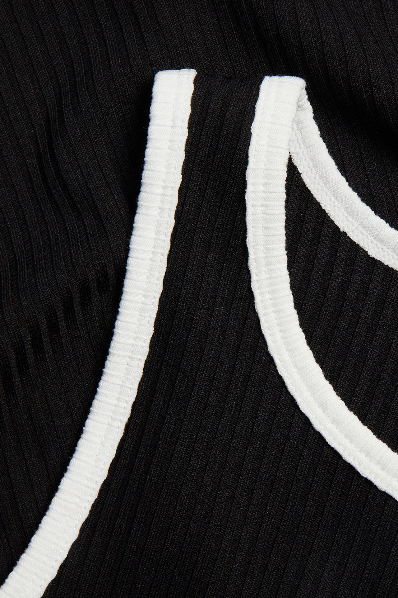 Nærbilde av en svart ribbestrikket topp med hvite kontrastkanter.