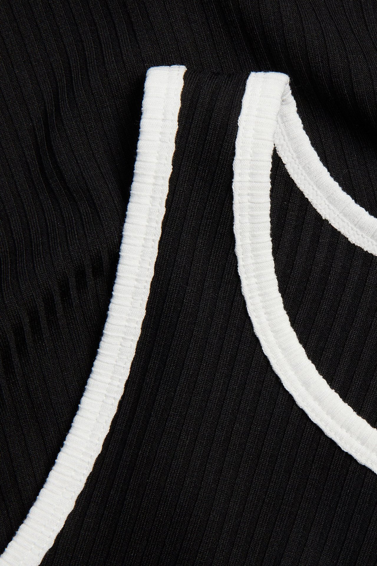 Zbliżenie czarnej prążkowanej koszulki na ramiączkach z białymi kontrastowymi brzegami.