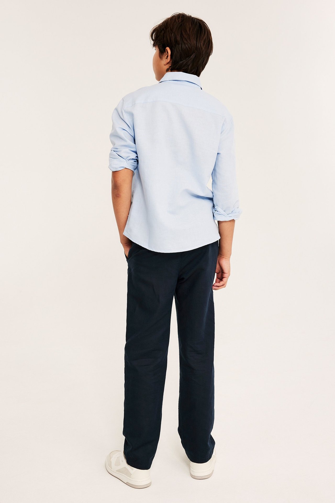 Widok z tyłu dziecka w ciemnoniebieskich prostych spodniach z lnu i jasnoniebieskiej koszuli.