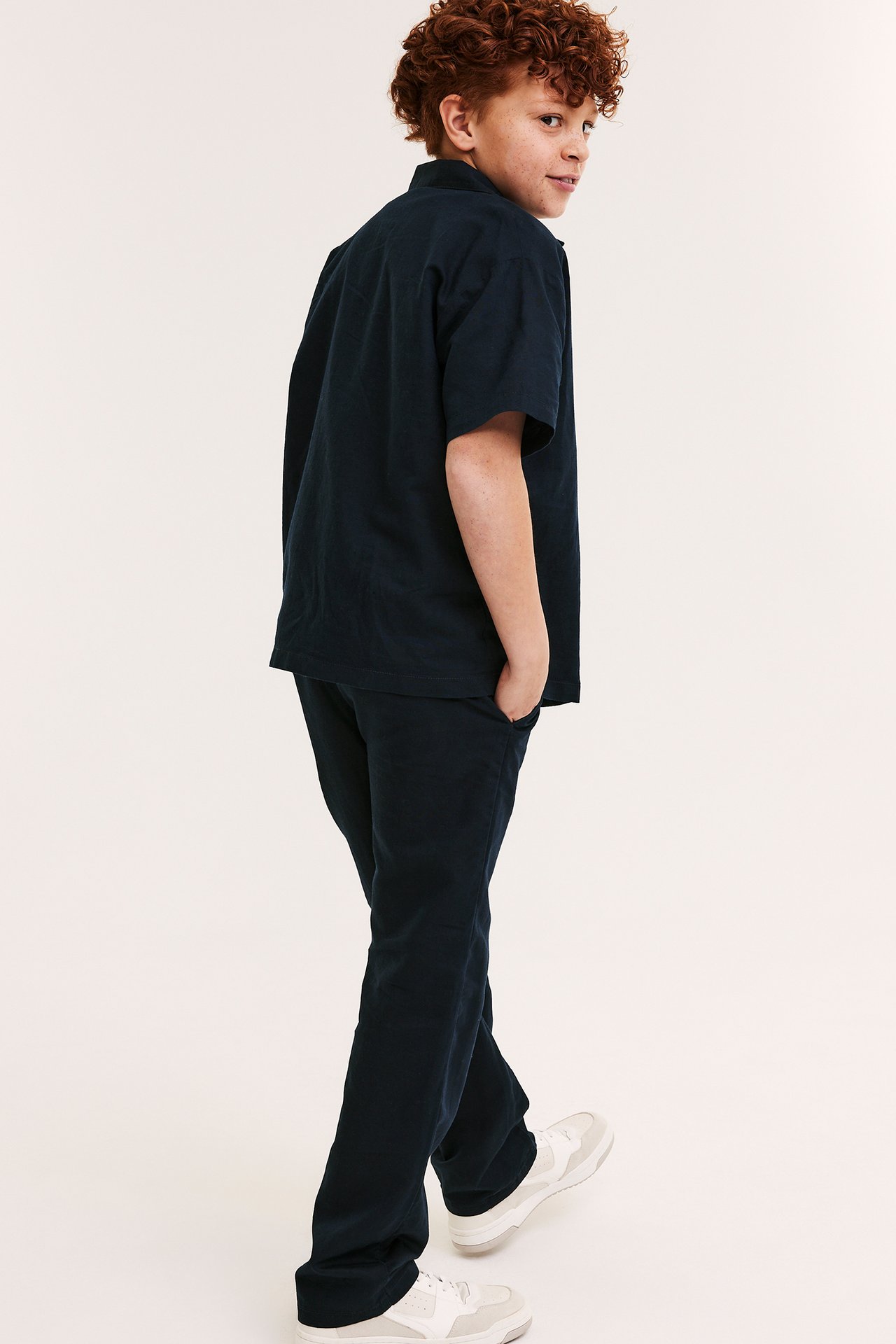 Sidovy av ett barn som bär mörkblå linneblandade byxor med matchande skjorta och vita sneakers.