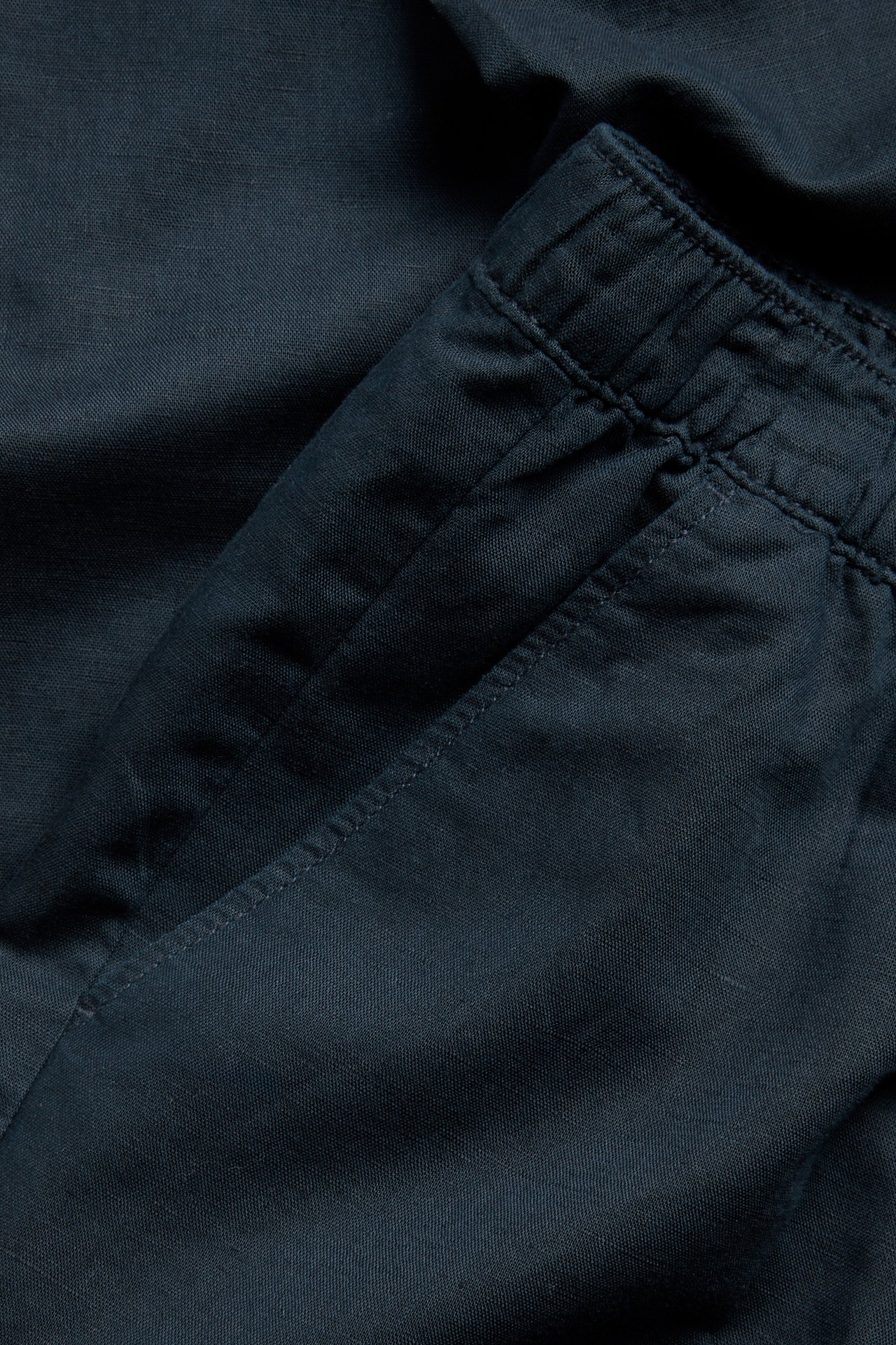 Nærbilde av mørkeblå linblandingsbukse med elastisk midje og sidelomme.