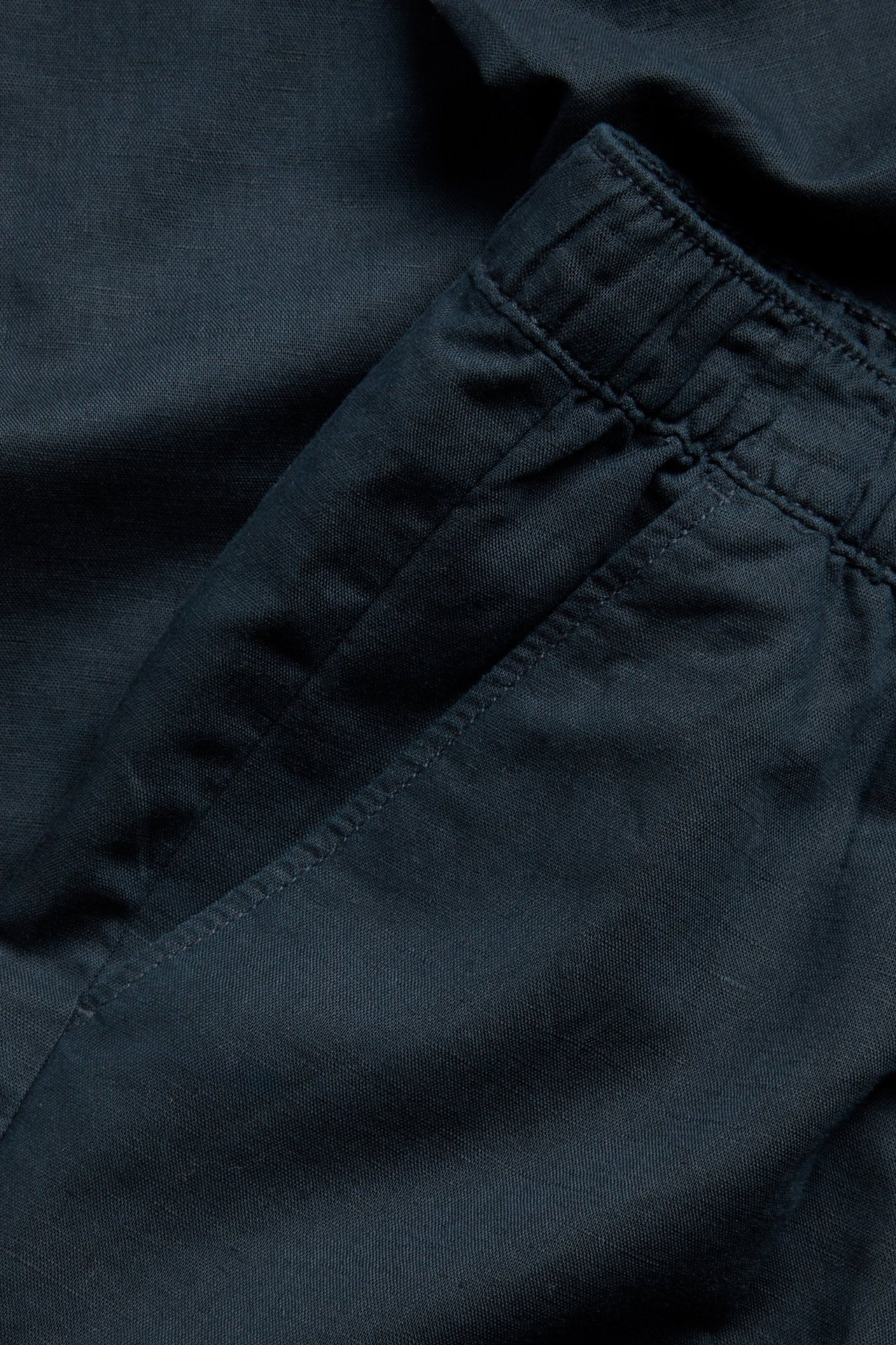 Zbliżenie ciemnoniebieskich spodni z mieszanki lnu z elastycznym pasem i kieszenią boczną.