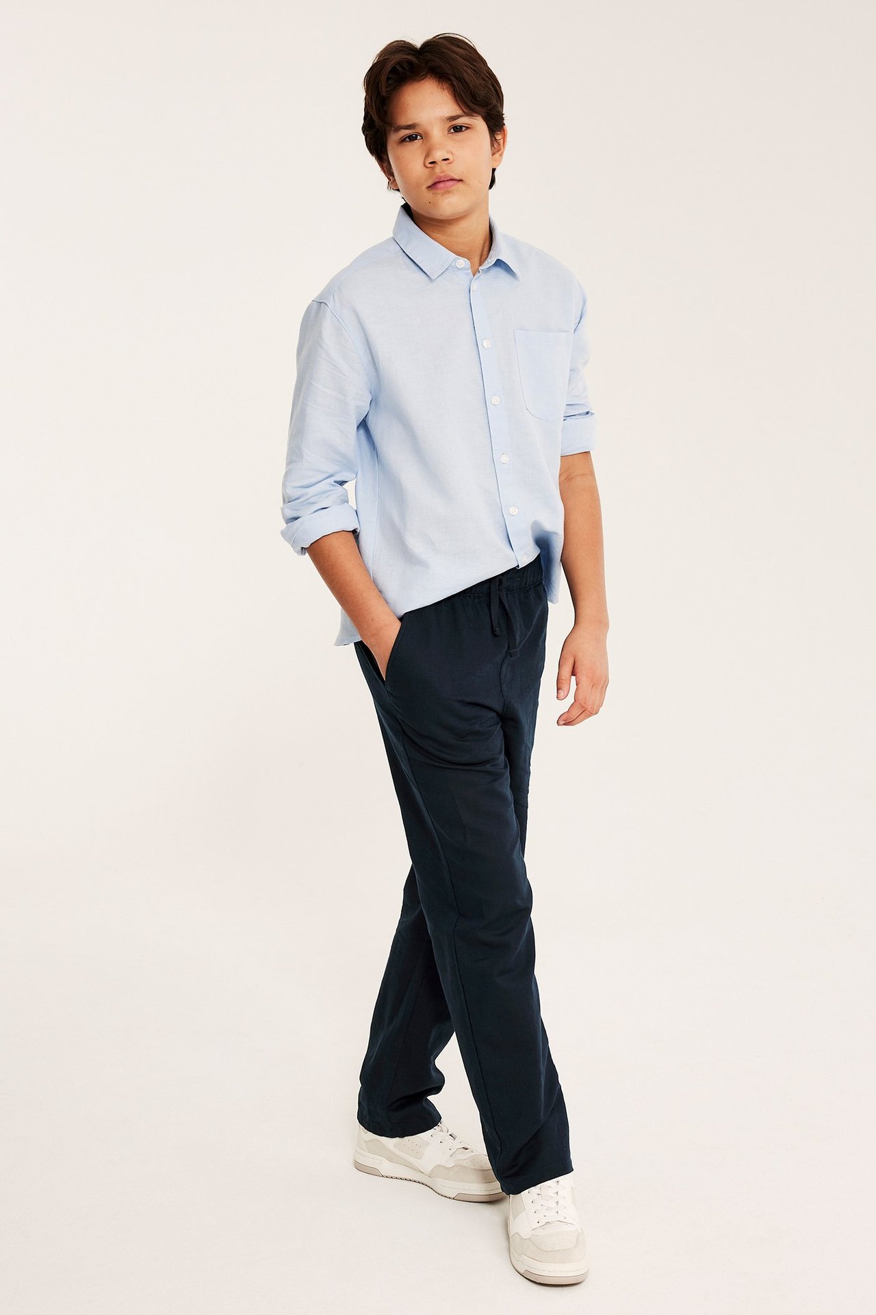 Edestä: poika yllään tummansiniset pellavasekoitehousut kiristysnyörillä, vaaleansininen pellavapaita ja valkoiset tennarit.