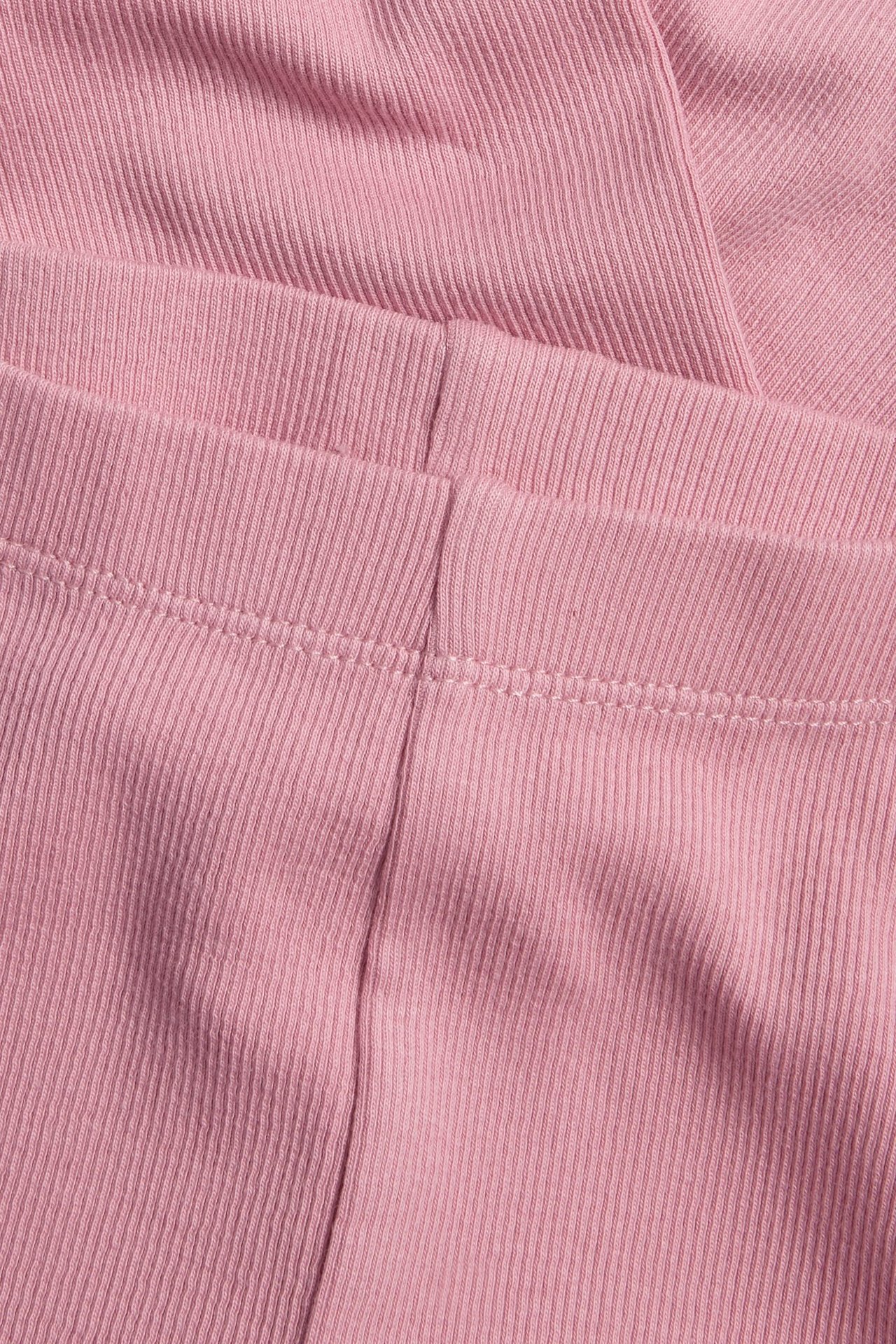 Zbliżenie na jasnoróżowe prążkowane legginsy z widocznymi szwami.