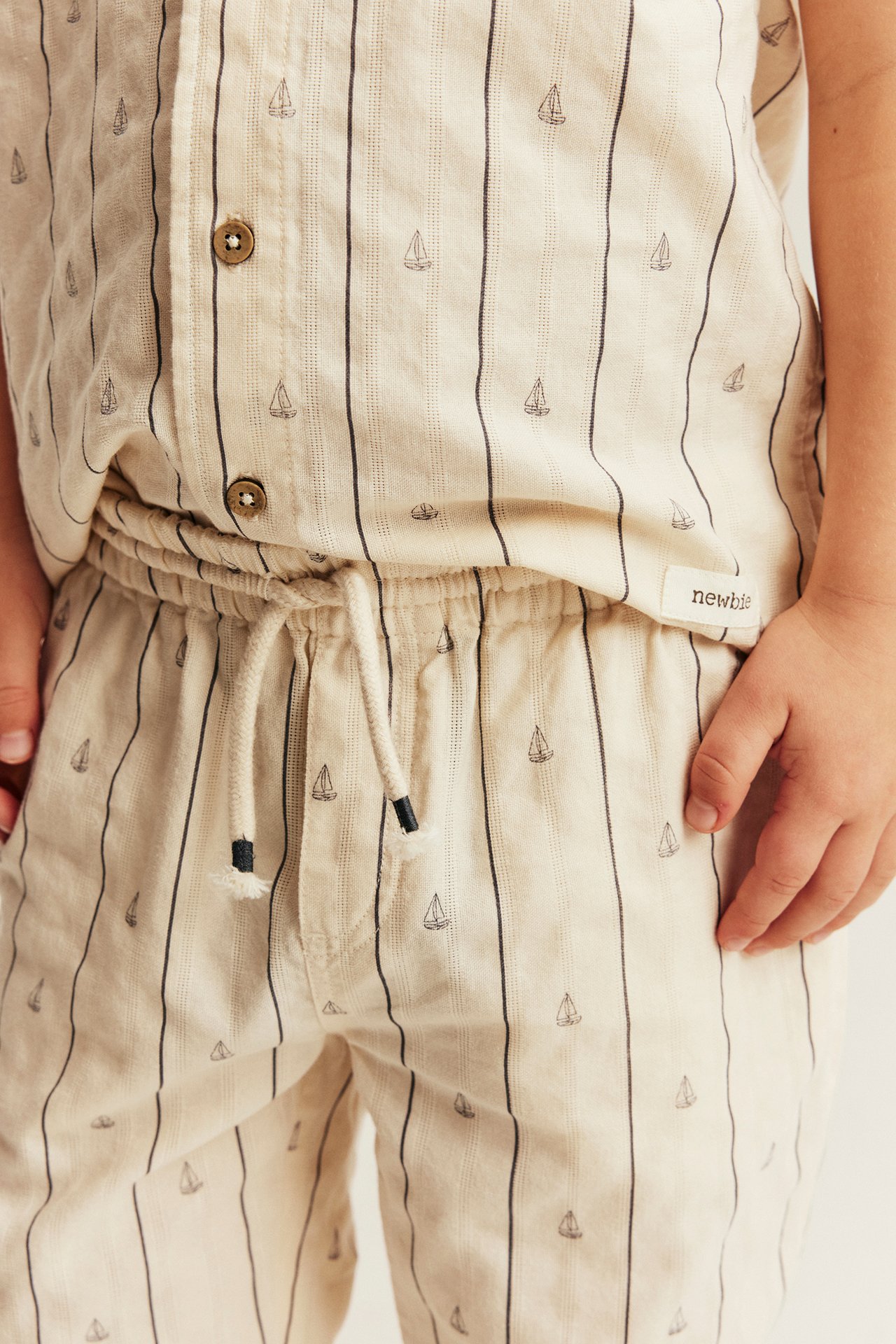 Barn bærer hvite bomullsbukser med striper, seilbåter, snøring i livet og matchende topp.