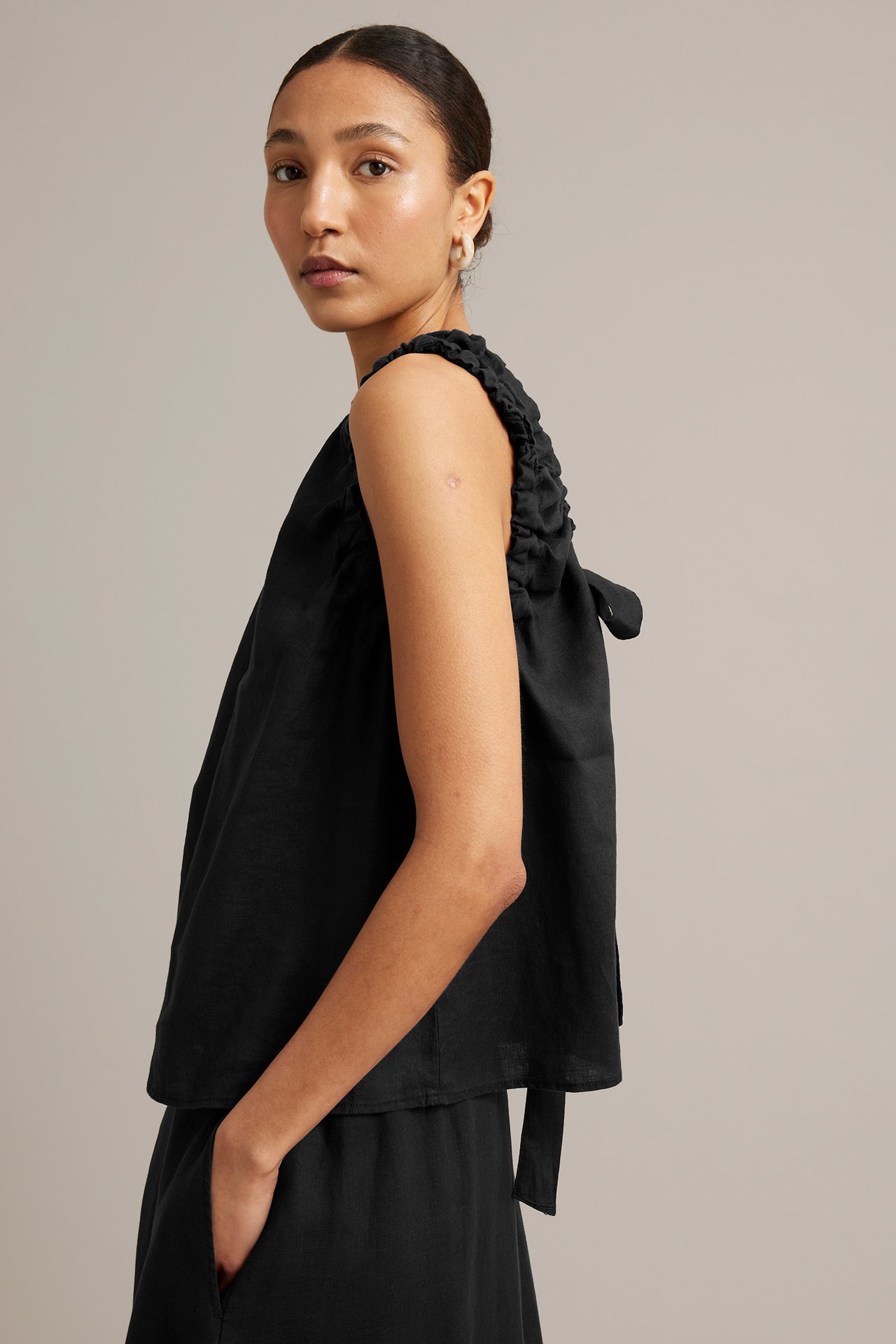 Sidovy av kvinna i svart linnetopp med knytband i ryggen, matchande svarta byxor.