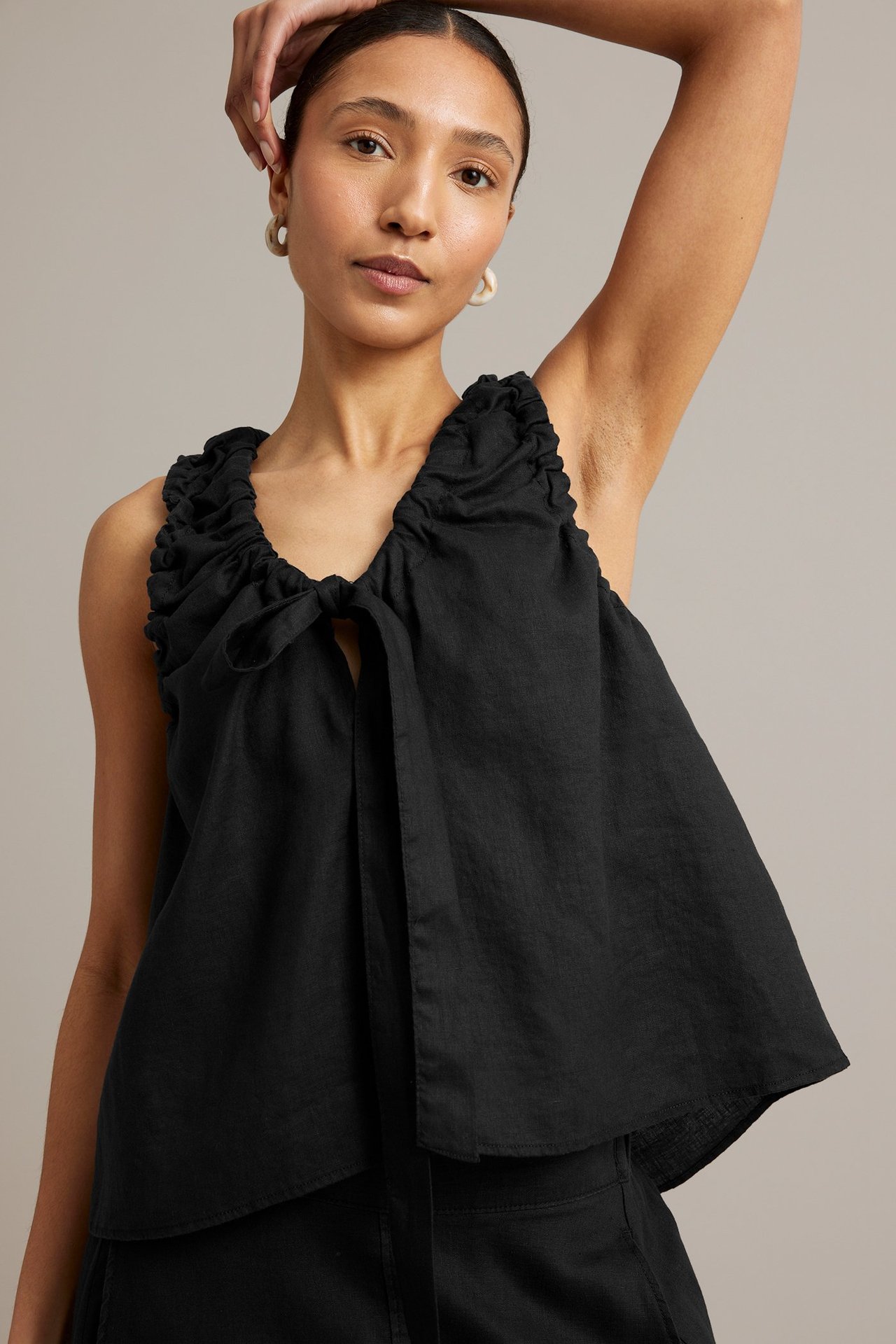 Framifrån, kvinna i svart linnetopp med knytning i halsen, volanger och ljusa ringörhängen.