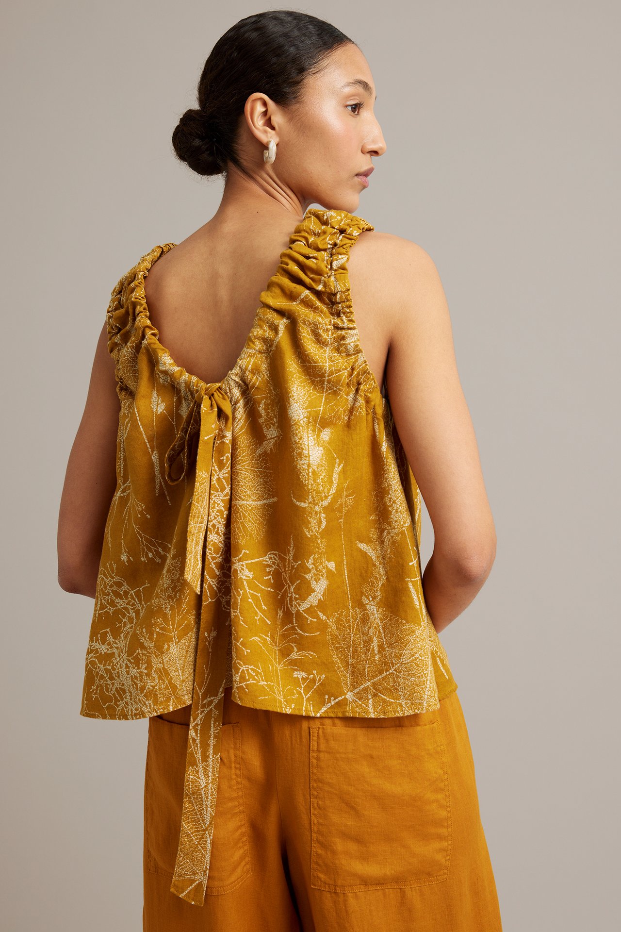 Ryggvy av kvinna i gul blommig linnetopp med rynkade axelband, knyt bak, och matchande byxor.